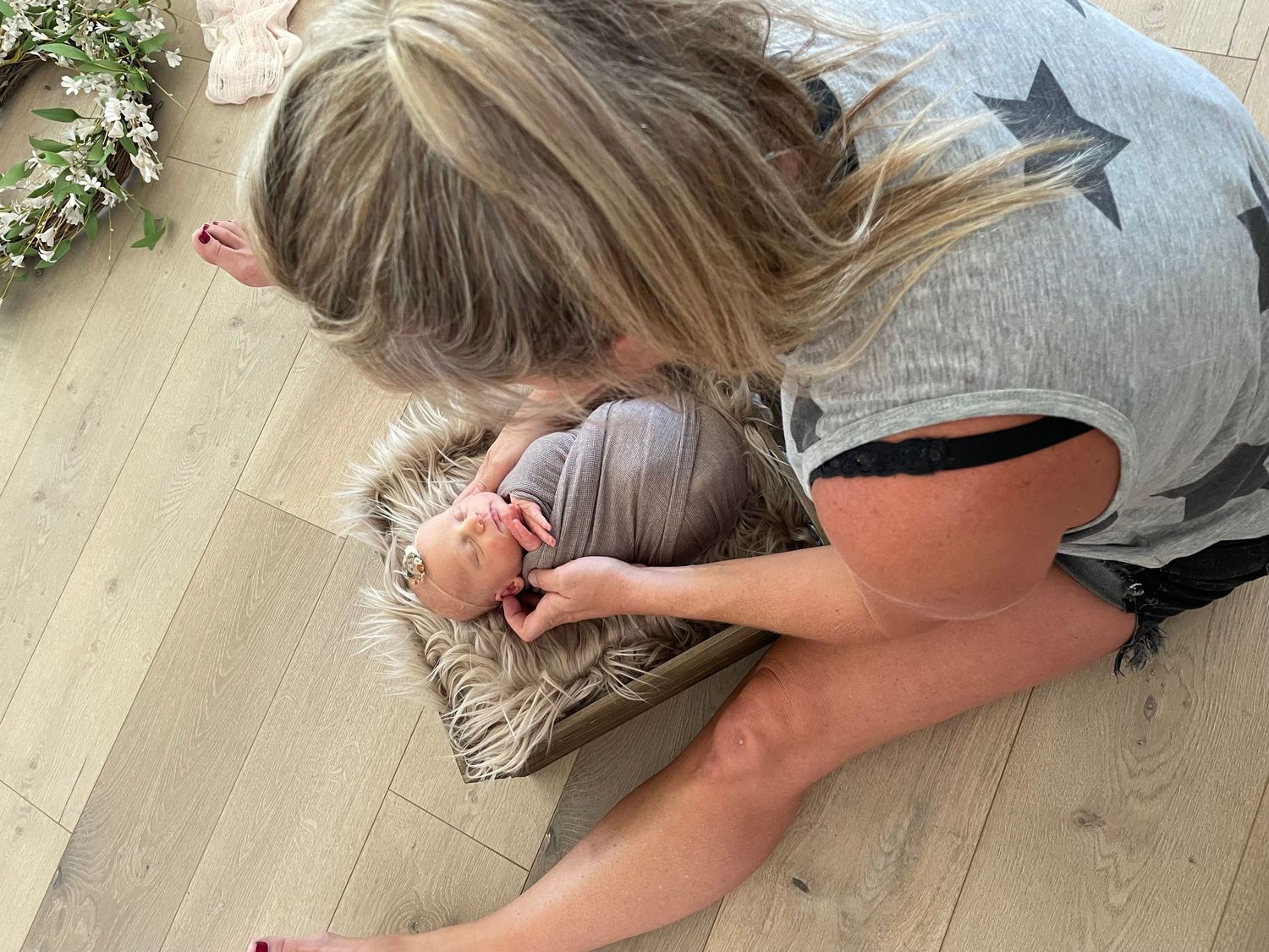 Woman kneeling on hardwood floor, tenderly cradling a newborn baby wrapped in soft blankets.
