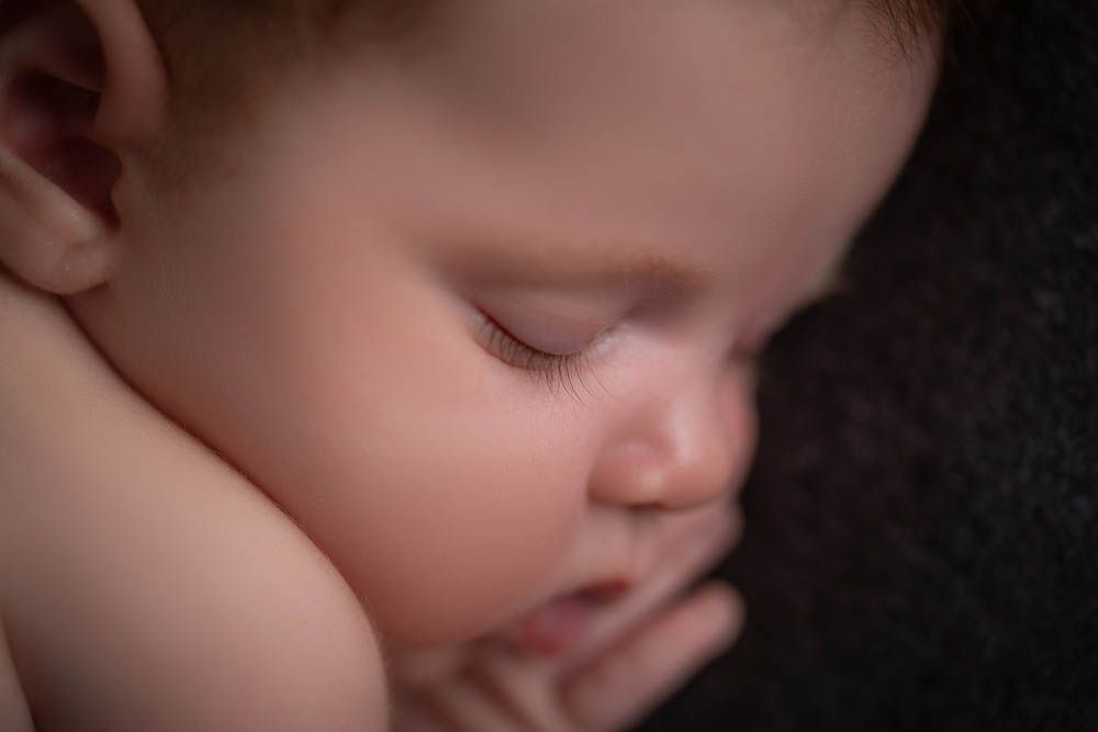 Close-up of a peaceful sleeping newborn baby with delicate features resting on a dark background.