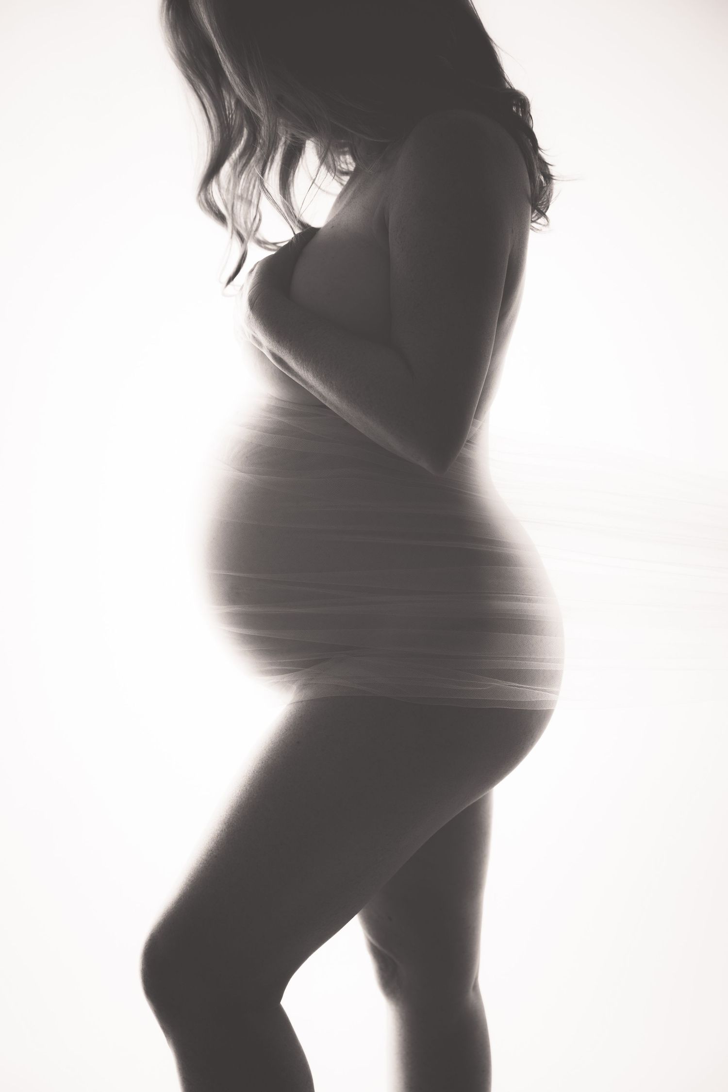 Black and white silhouette of a pregnant woman cradling her baby bump against a bright white background.