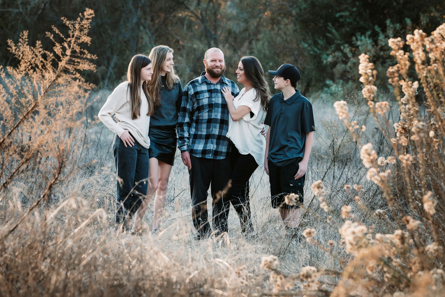 Family of five standing among tall dried wildflowers in golden hour light.