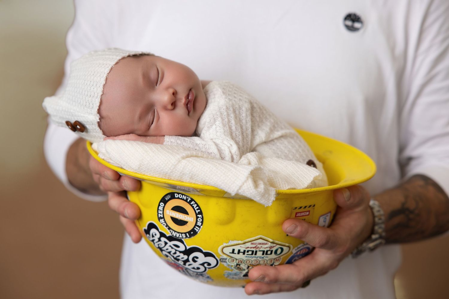Sleeping newborn baby wrapped in white swaddle resting in a yellow Maruchan ramen bowl held by an adult.