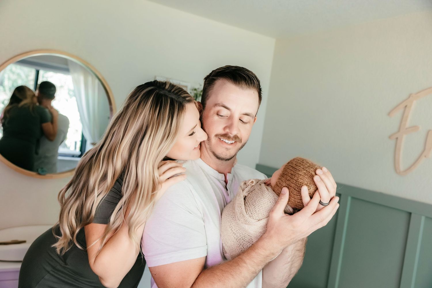 A couple shares a tender moment holding their newborn baby in a softly decorated nursery room.