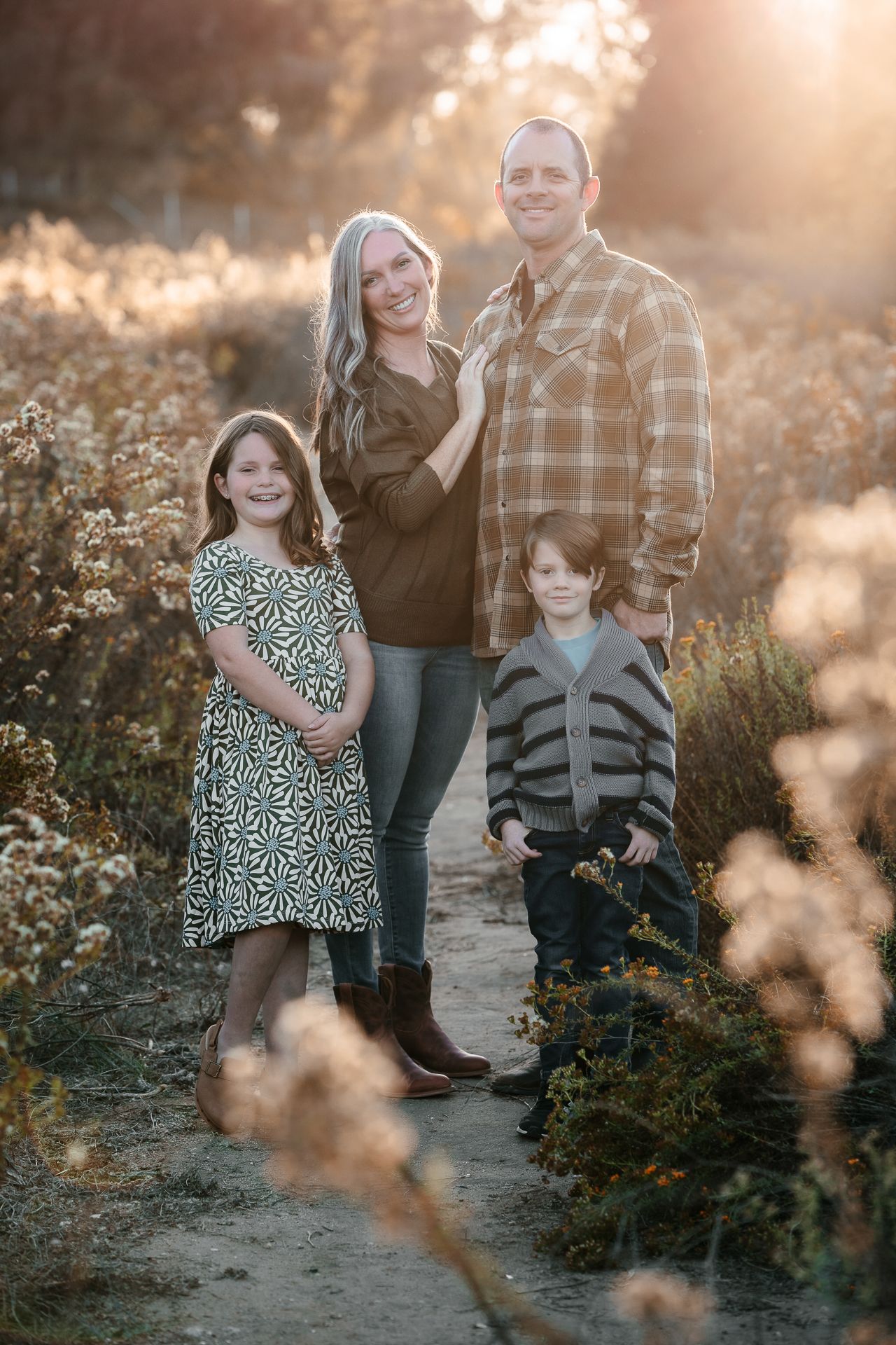 Family of four standing on sunlit nature path surrounded by wildflowers during golden hour in Bonsall, near Fallbrook, & Temecula