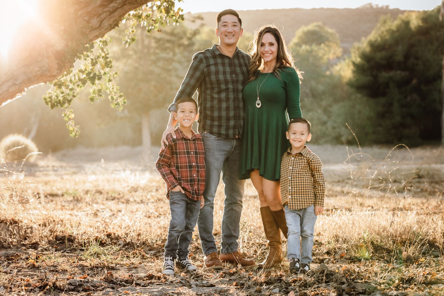 Family of four stands together in a sunlit golden field during autumn family portrait.