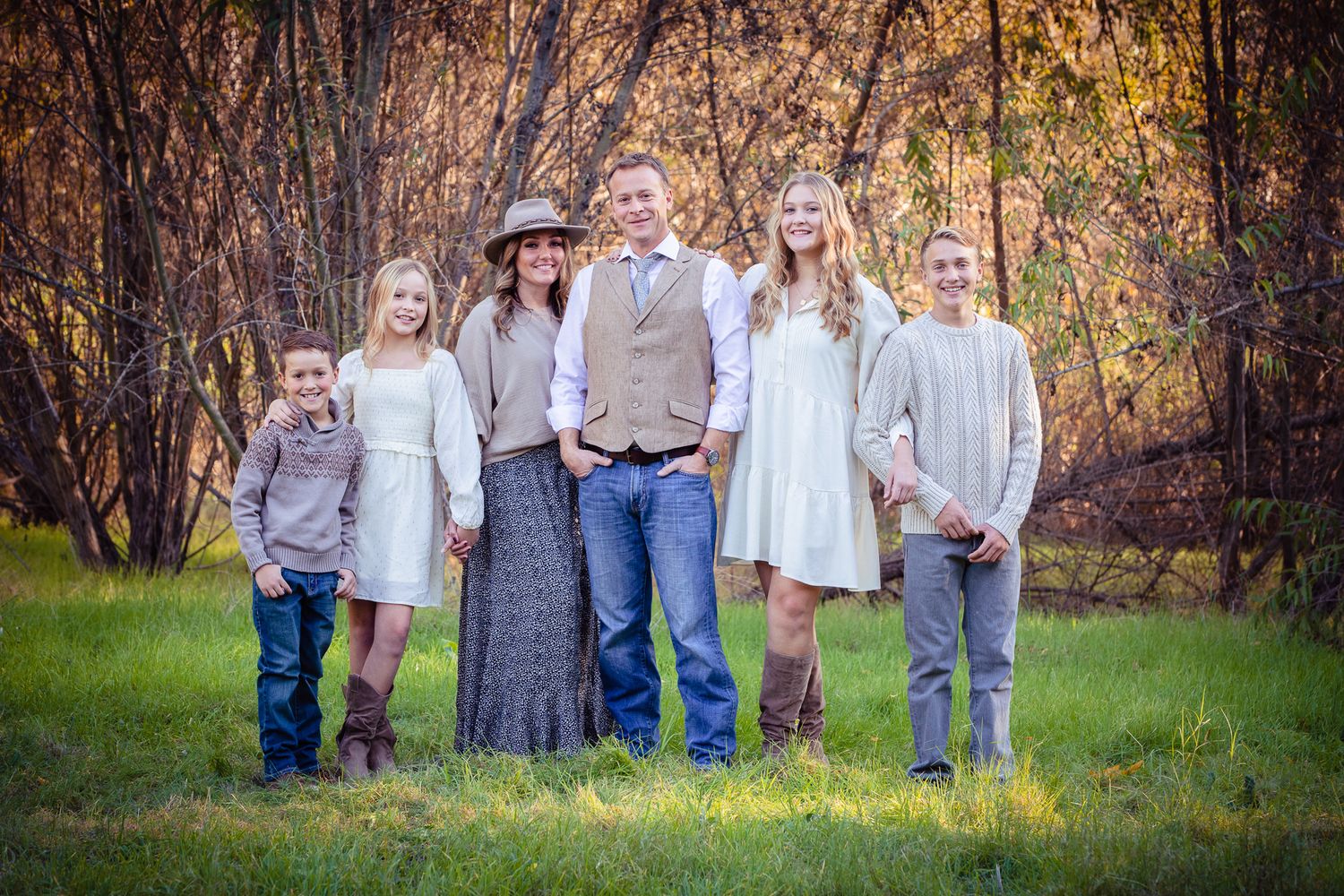 Family of six stands together smiling in a green meadow with autumn trees behind them in Fallbrook near Bonsall
