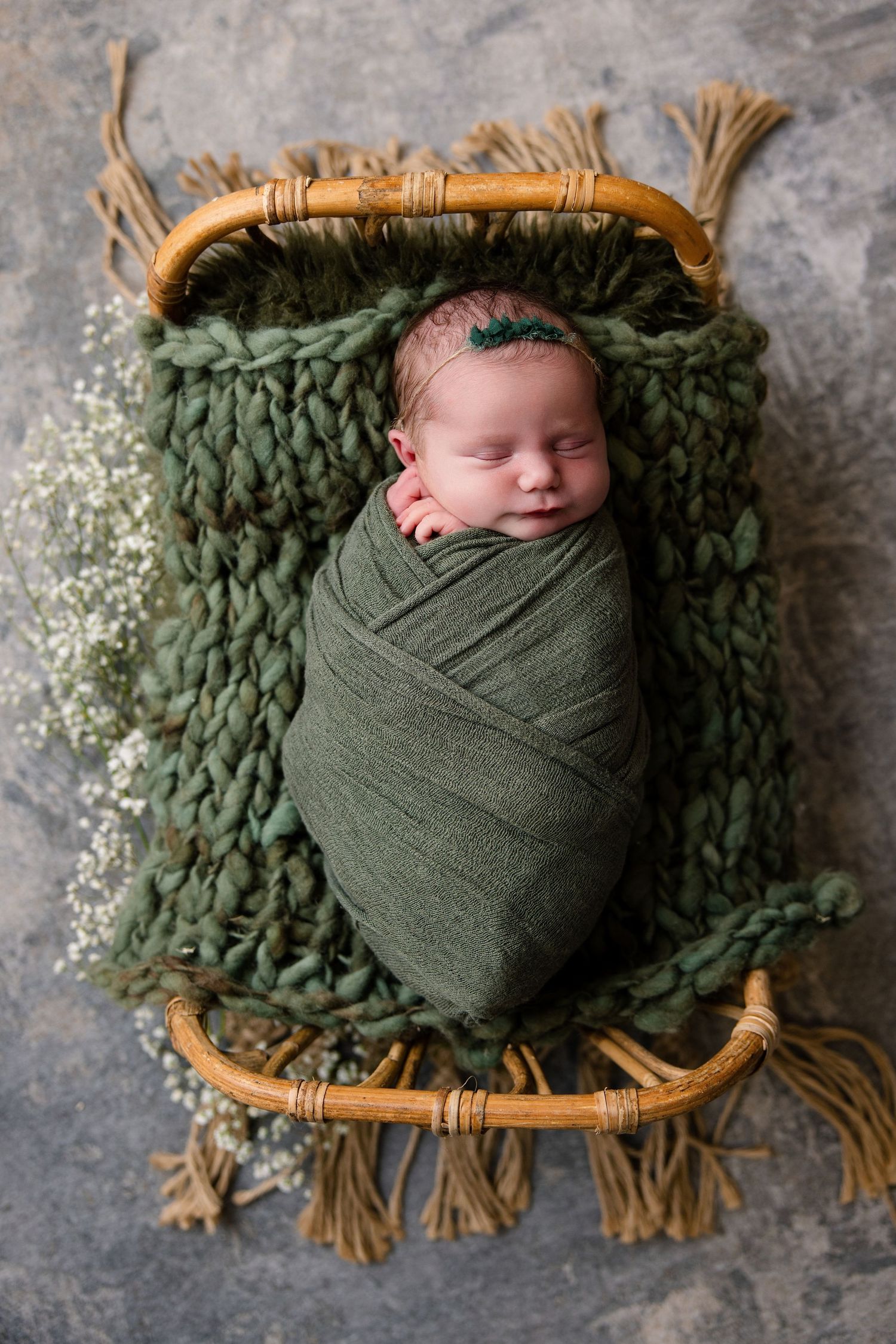 Posed Newborn baby wrapped in green swaddle sleeping in small rattan crib with knit blanket in Bonsall Studio in Fallbrook/Bonsall