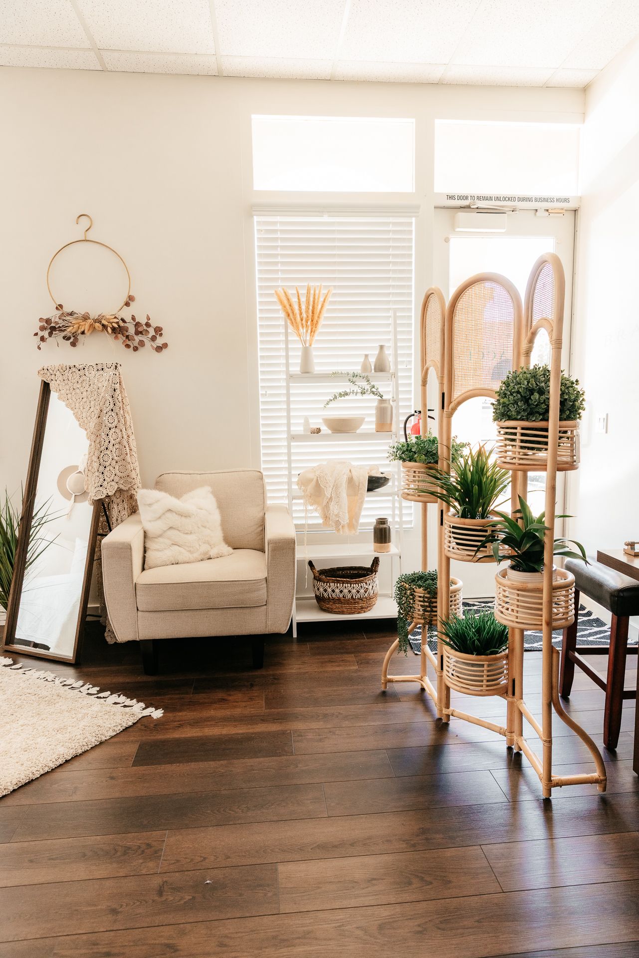 Bohemian living room with rattan plant stand, lush greenery, cream armchair, macrame decor, and warm wood floors. in the Bonsall Studio near