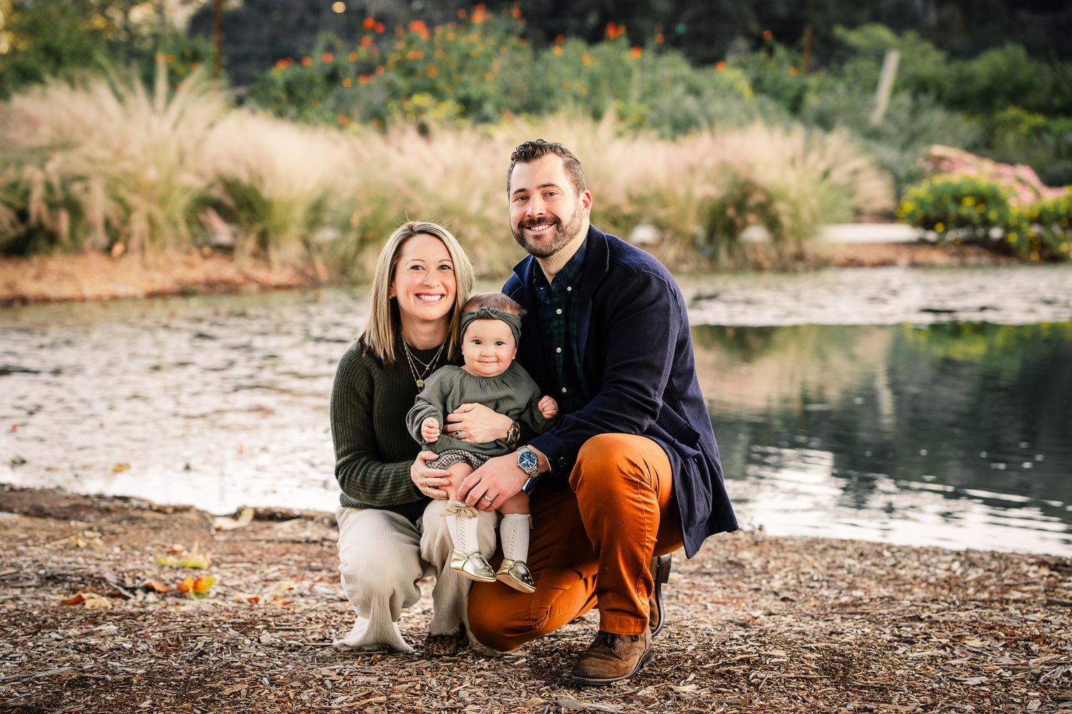 Young couple with baby posing by pond in colorful autumn garden.