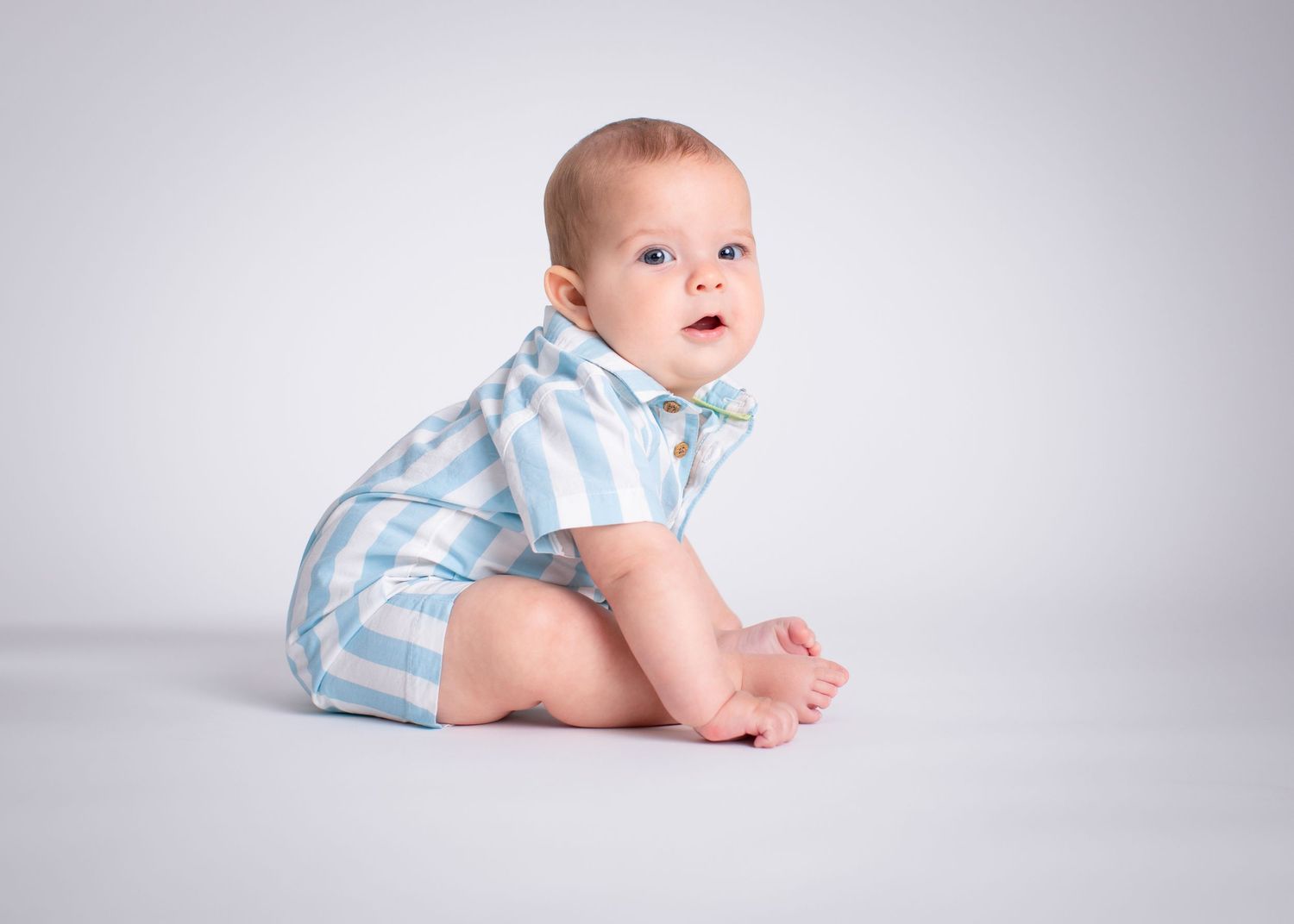 A baby wearing light blue and white striped clothing lies on a white backdrop in a series of connected poses.