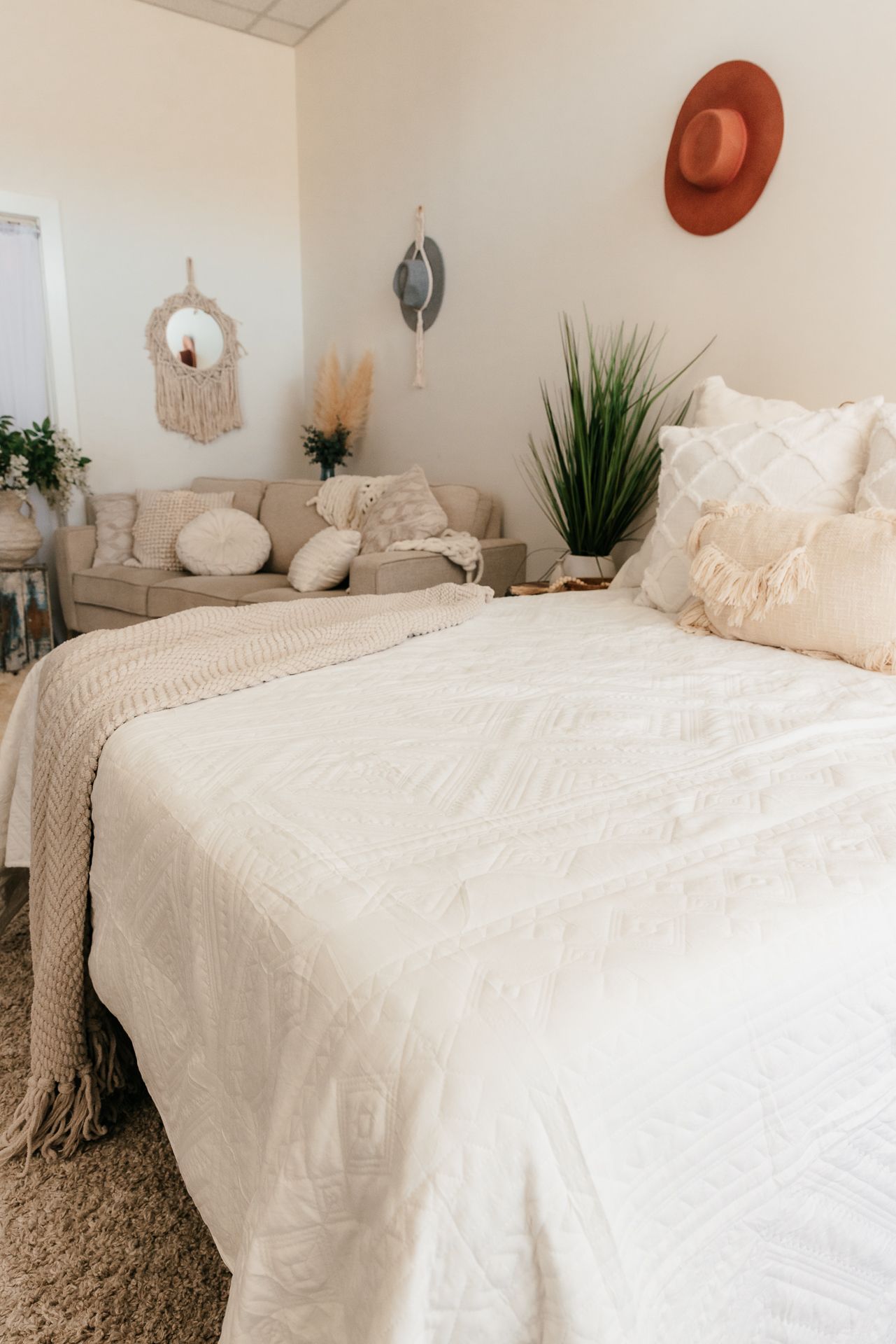 Boho bedroom with white tufted bedding, knit throw, cream sofa, and terracotta hat wall decor. in the Bonsall Studio near Fallbrook, Vista,