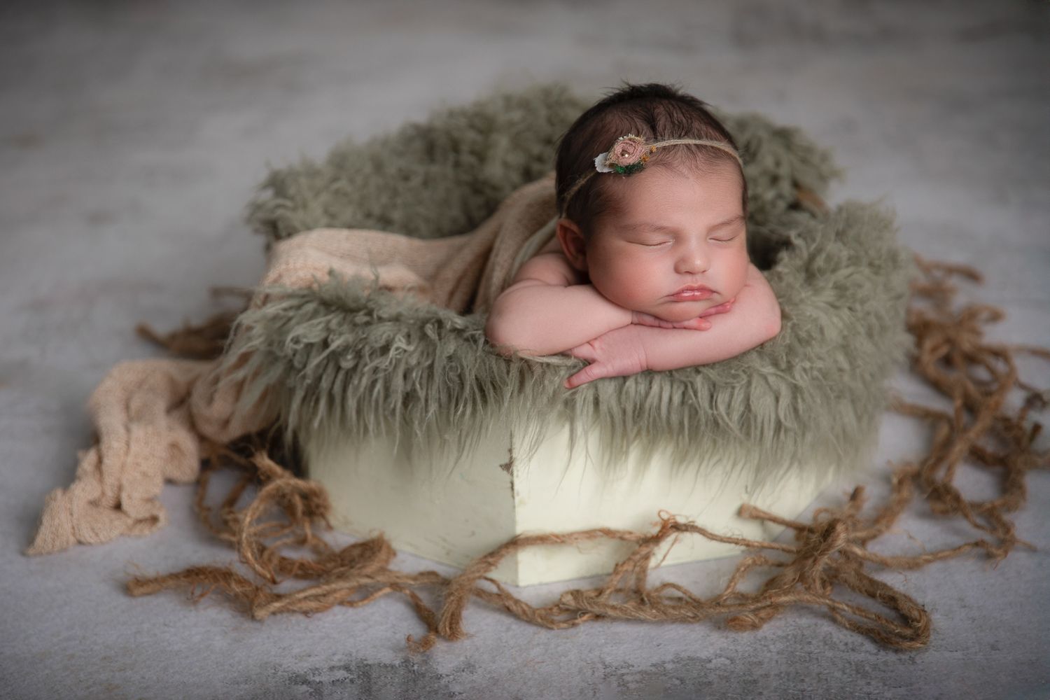 Sleeping newborn baby posed with chin on hands in a round wooden bowl lined with green fluffy fur. vista newborn photographer