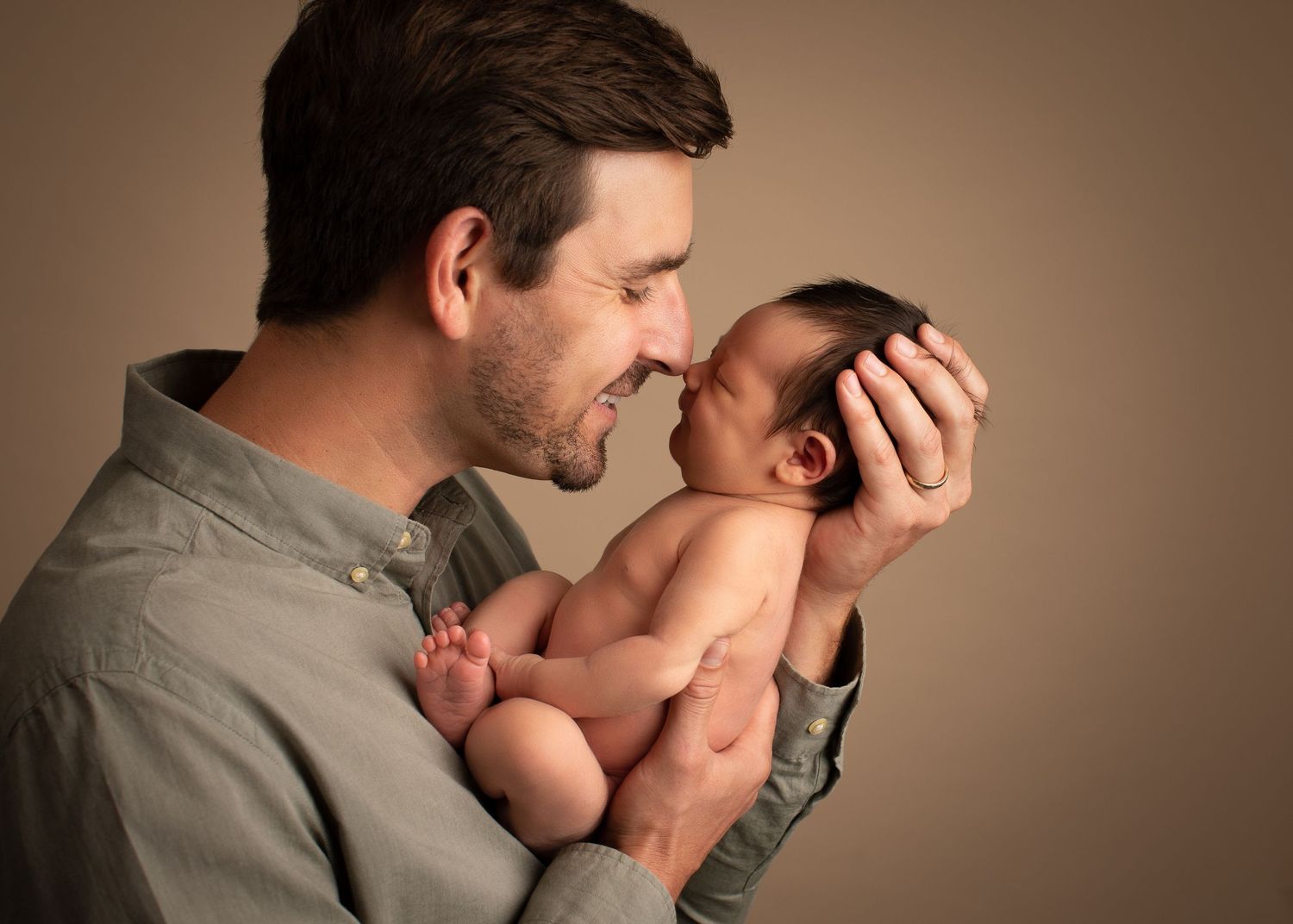 A smiling father tenderly holds his newborn baby close in a warm studio portrait.