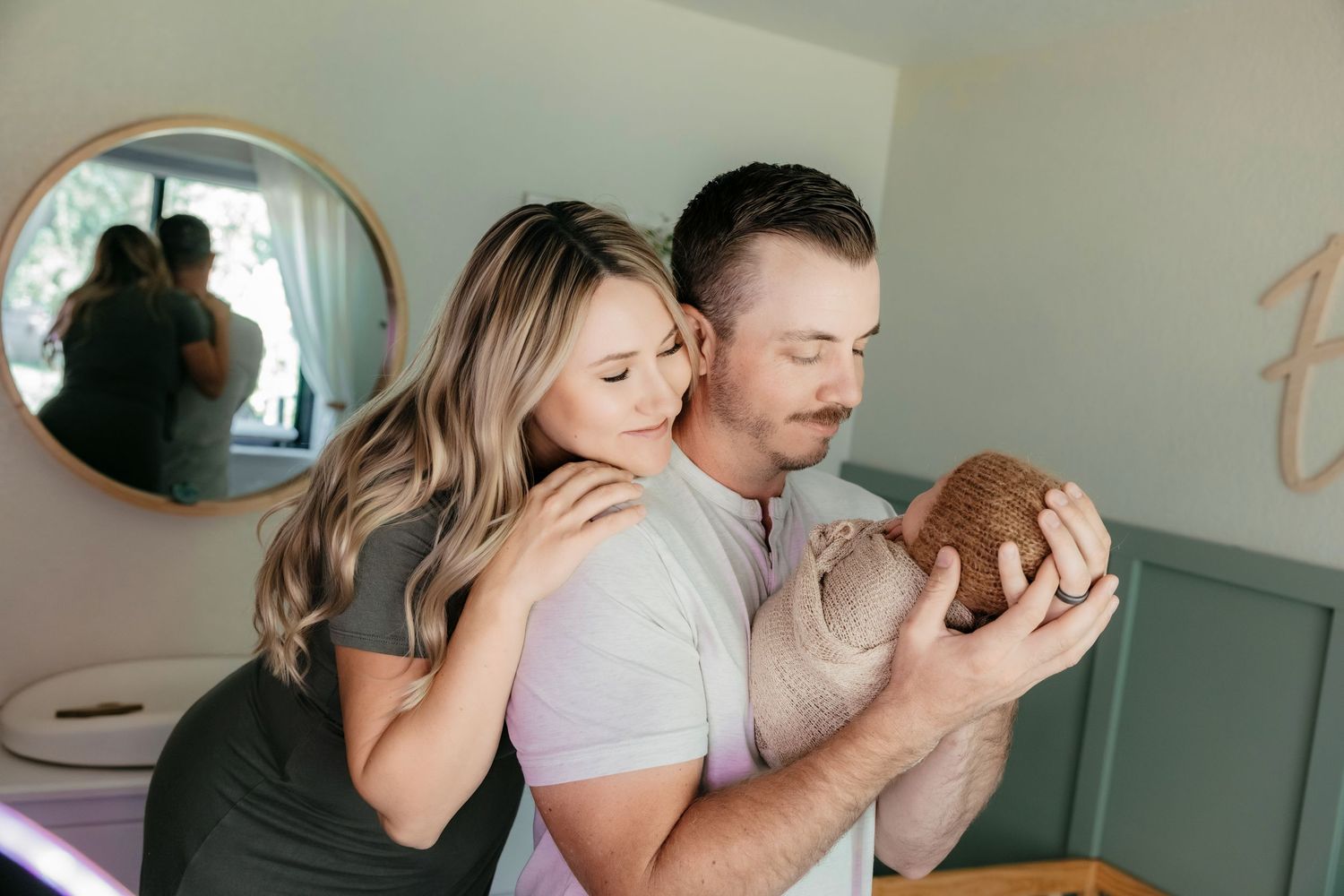 A couple tenderly holds their newborn baby in a softly decorated nursery room.