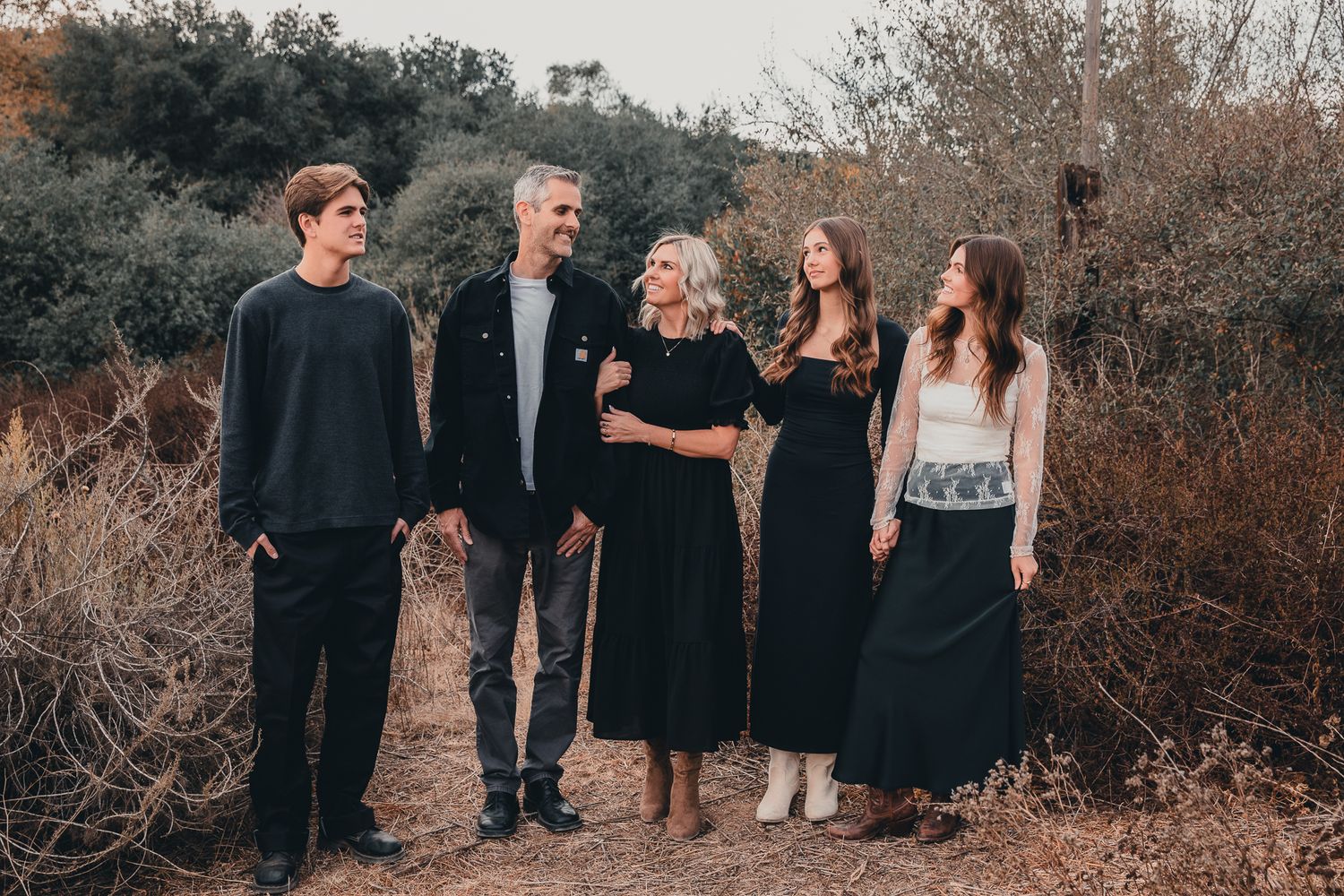 Family of five walking together on a brushy outdoor trail.