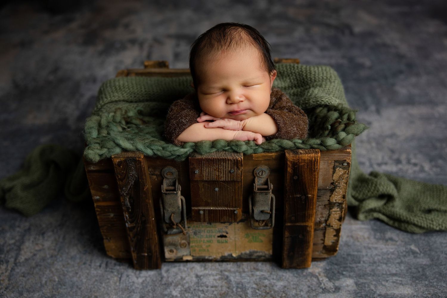 Sleeping newborn baby posed in a vintage wooden crate with green knit wrap for a professional newborn photo.