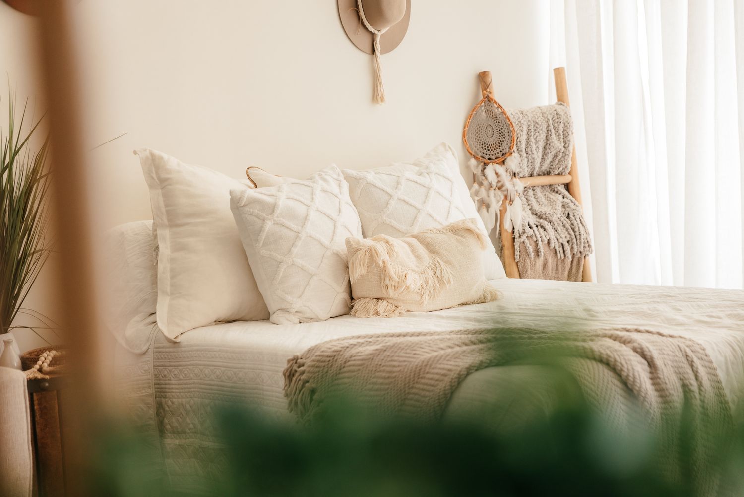 Close-up of boho bed with layered white pillows, knit throw, wooden ladder, and sheer curtains. in the Bonsall Studio near Fallbrook, Vista,