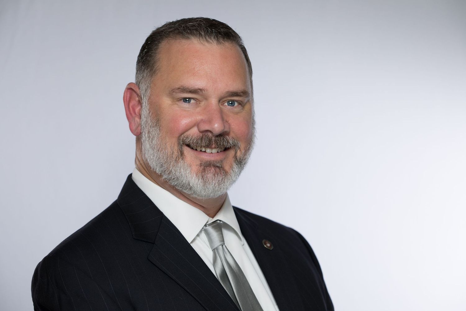 Professional headshot of a man with gray beard wearing a dark suit and gray tie against light background in the Bonsall Studio near Fallbroo