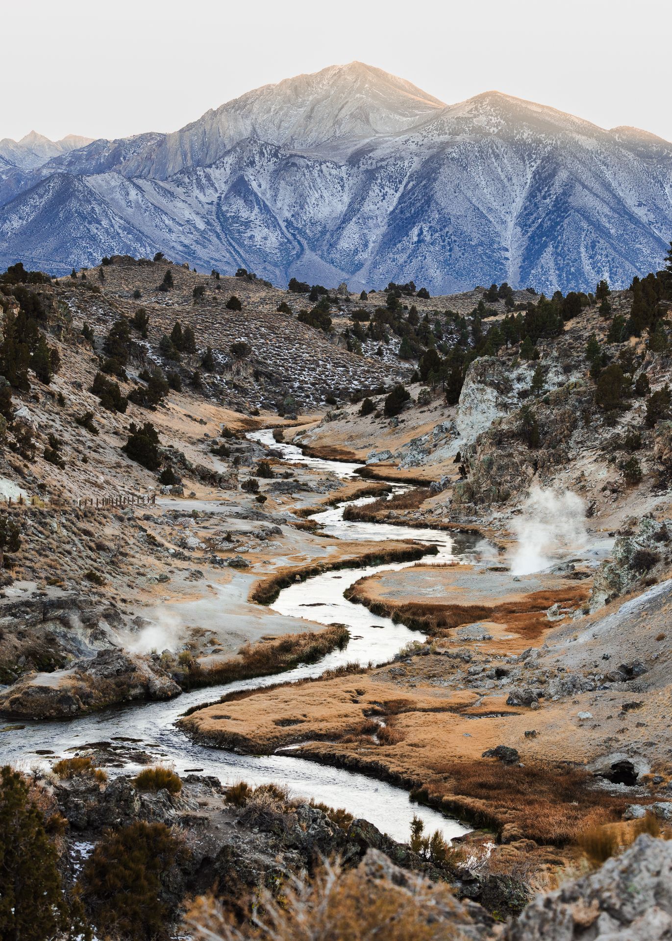 Panoramic view of a winding river cutting through mountainous terrain with thermal hot springs and snow-capped peaks. Geological Hot Springs