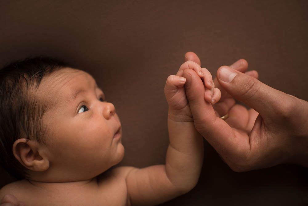 Newborn baby grasping an adult finger, looking up in a tender close-up portrait in the Bonsall Studio near Fallbrook, Vista, Oceanside &