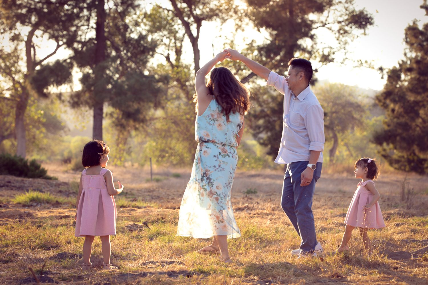 A joyful family dances together in a sunlit forest clearing during a golden hour photo session.