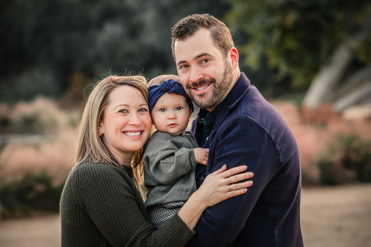 Smiling couple holding baby girl in autumn outdoor portrait session.