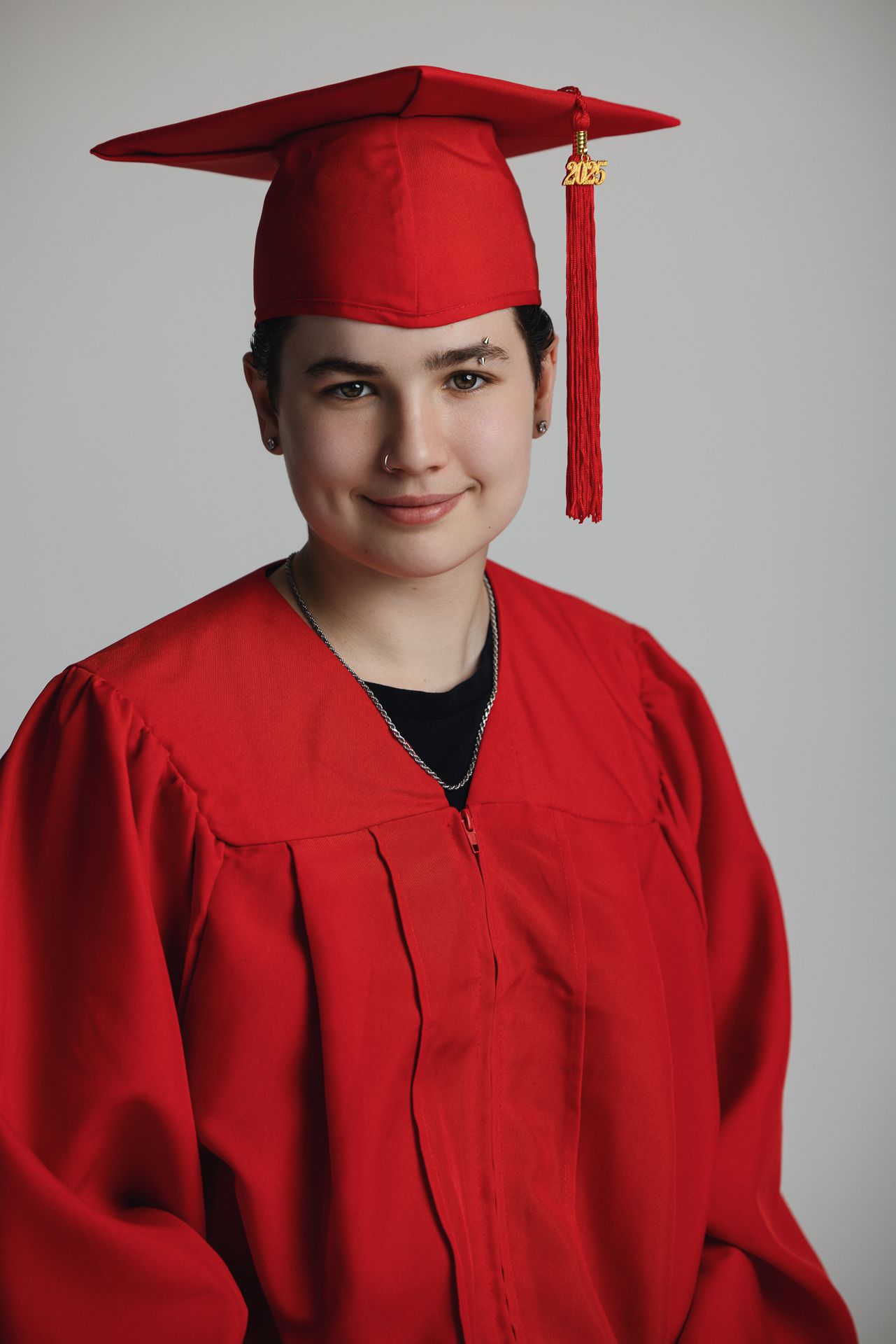 Young graduate smiling in red cap and gown against white background.
