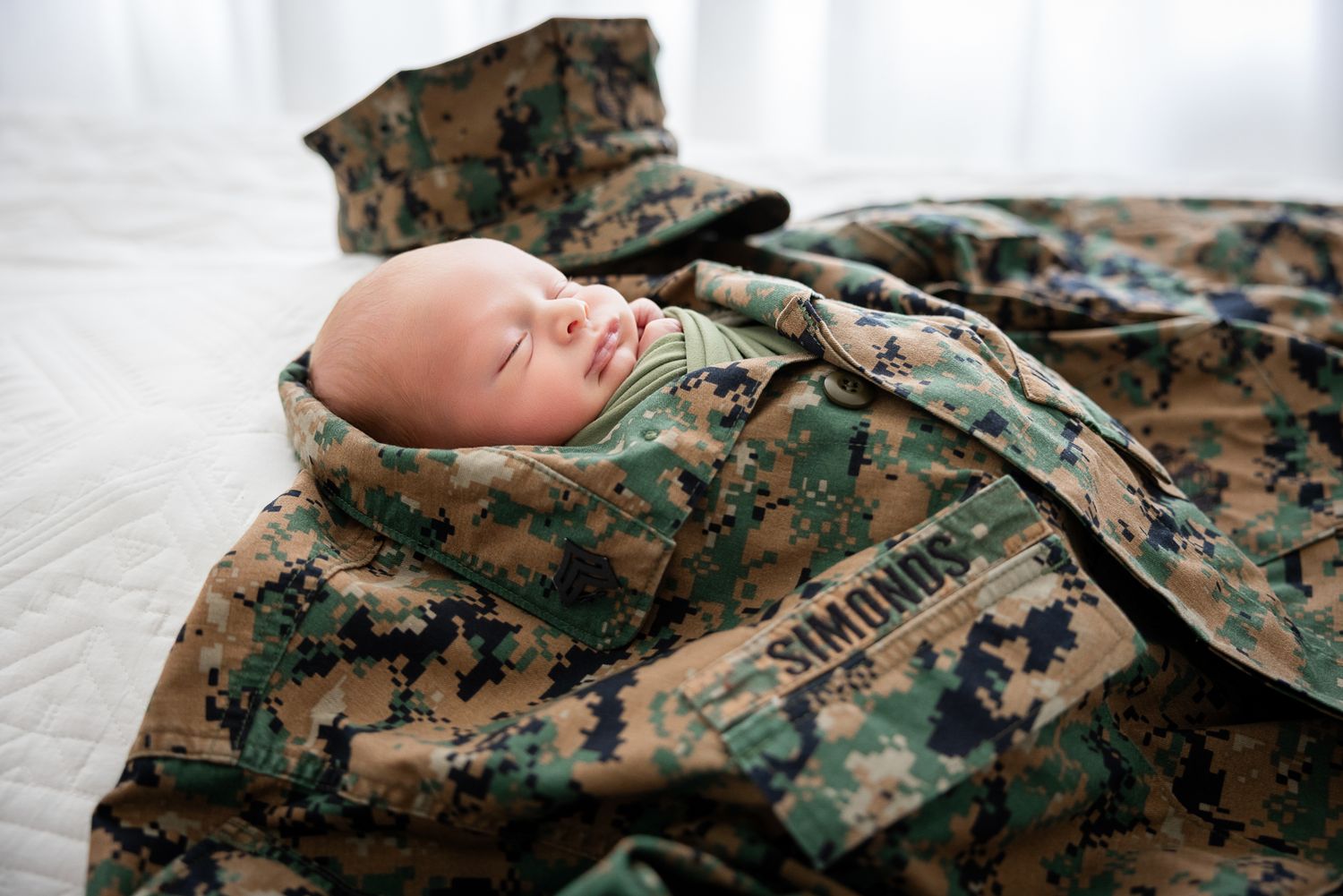 Newborn baby sleeping peacefully swaddled in a military camouflage uniform at The Studio Bonsall, near Camp Pendleton Oceanside
