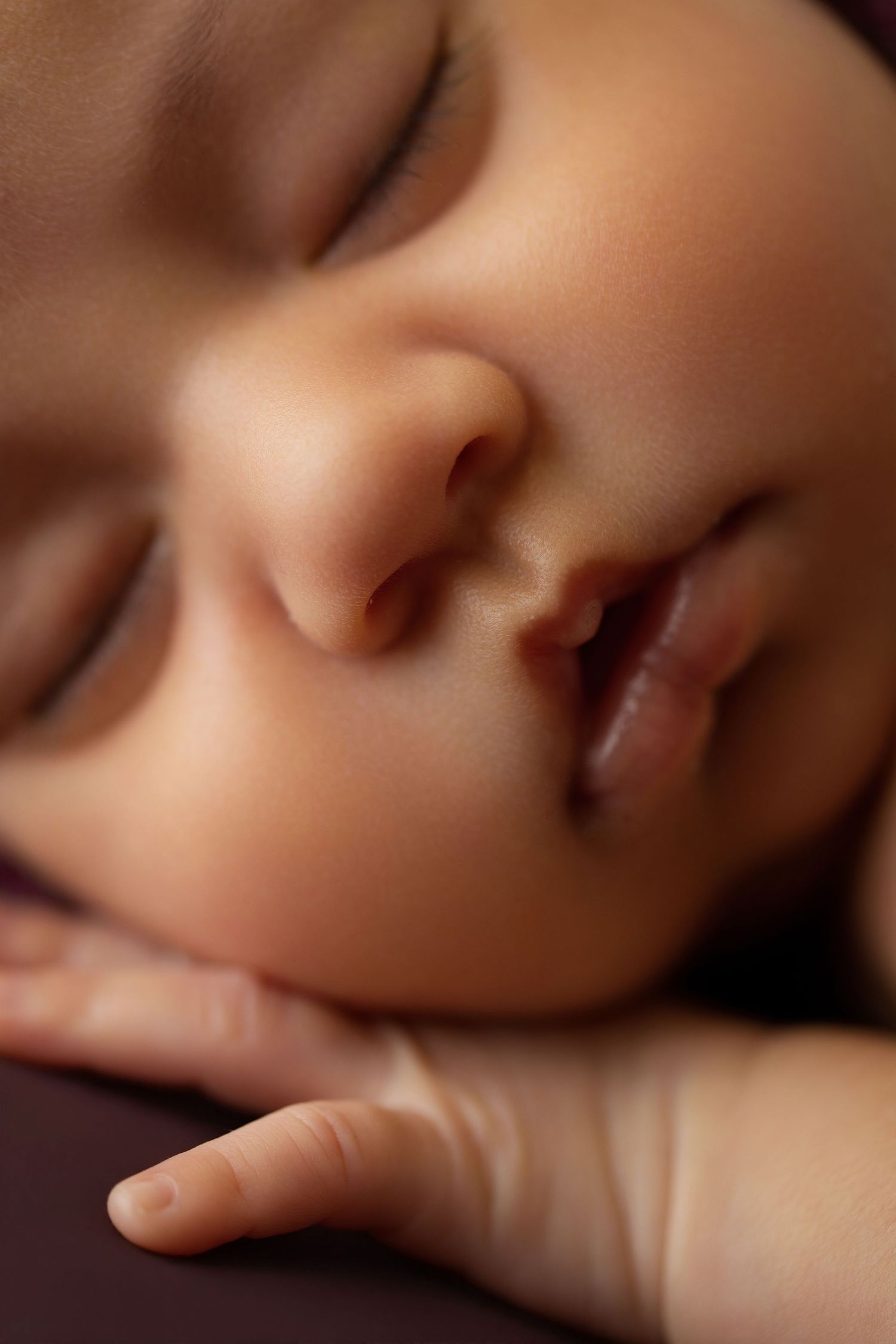 Close-up of a sleeping newborn baby with tiny fingers resting gently against their cheek.