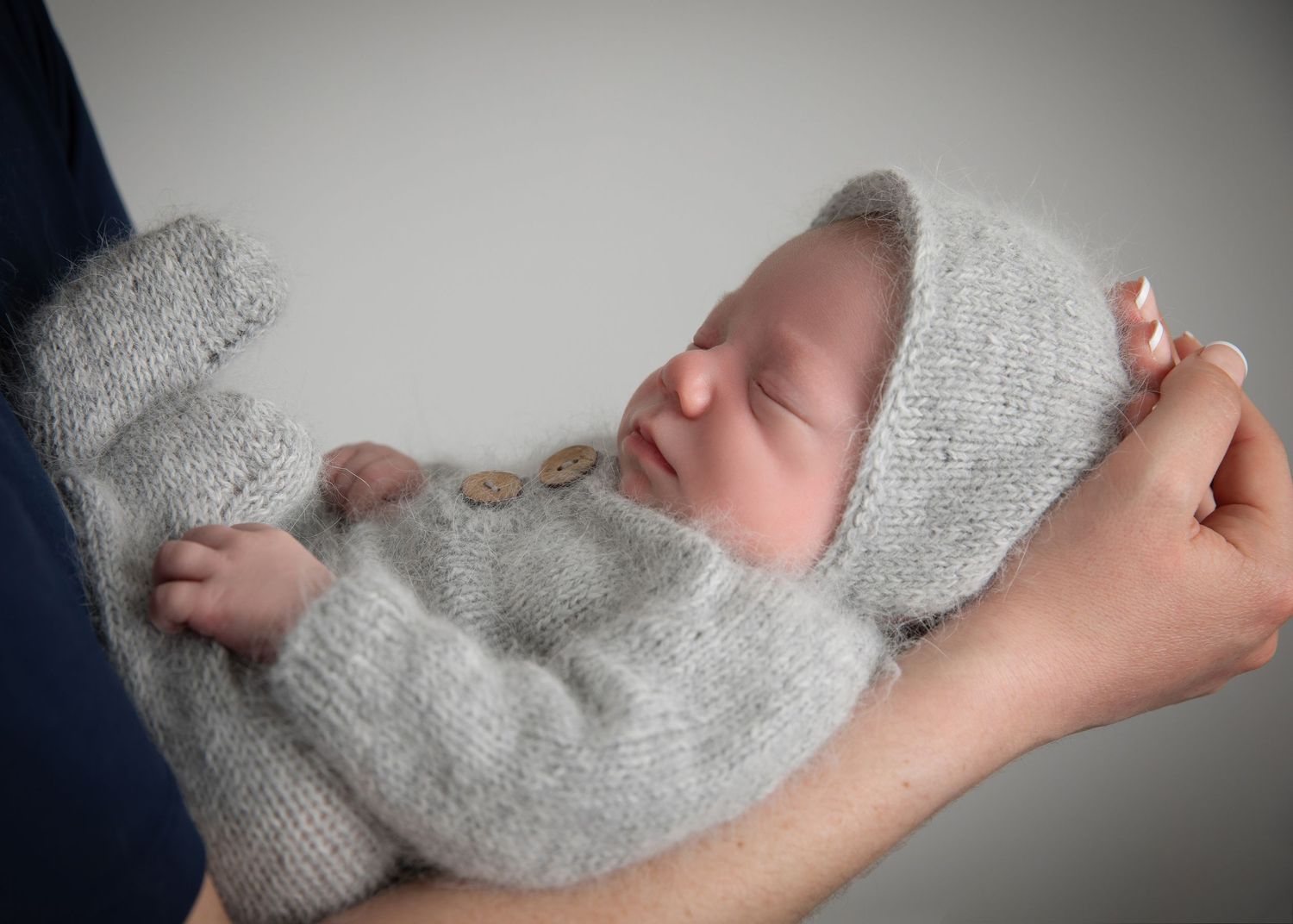 A sequence of photos showing a newborn wearing a soft gray sweater resting against a white background in his mothers arms.