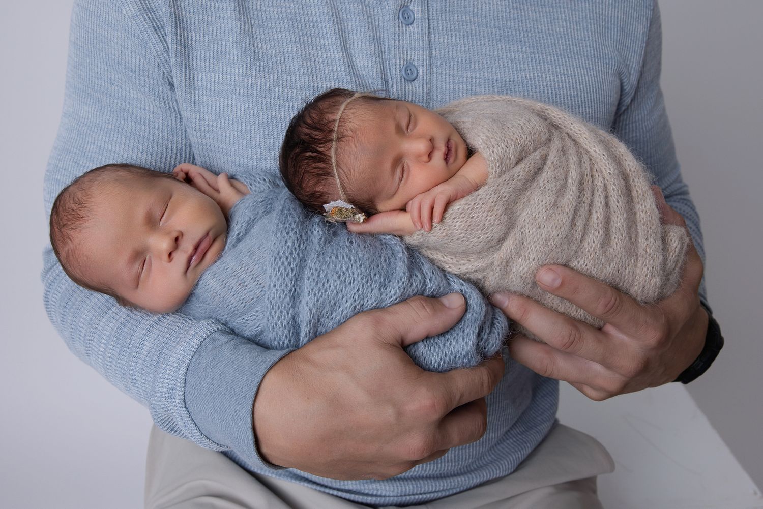 Father holding twin newborns swaddled in blue and beige wraps against white background at The Studio Bonsall, near Camp Pendleton Oceanside