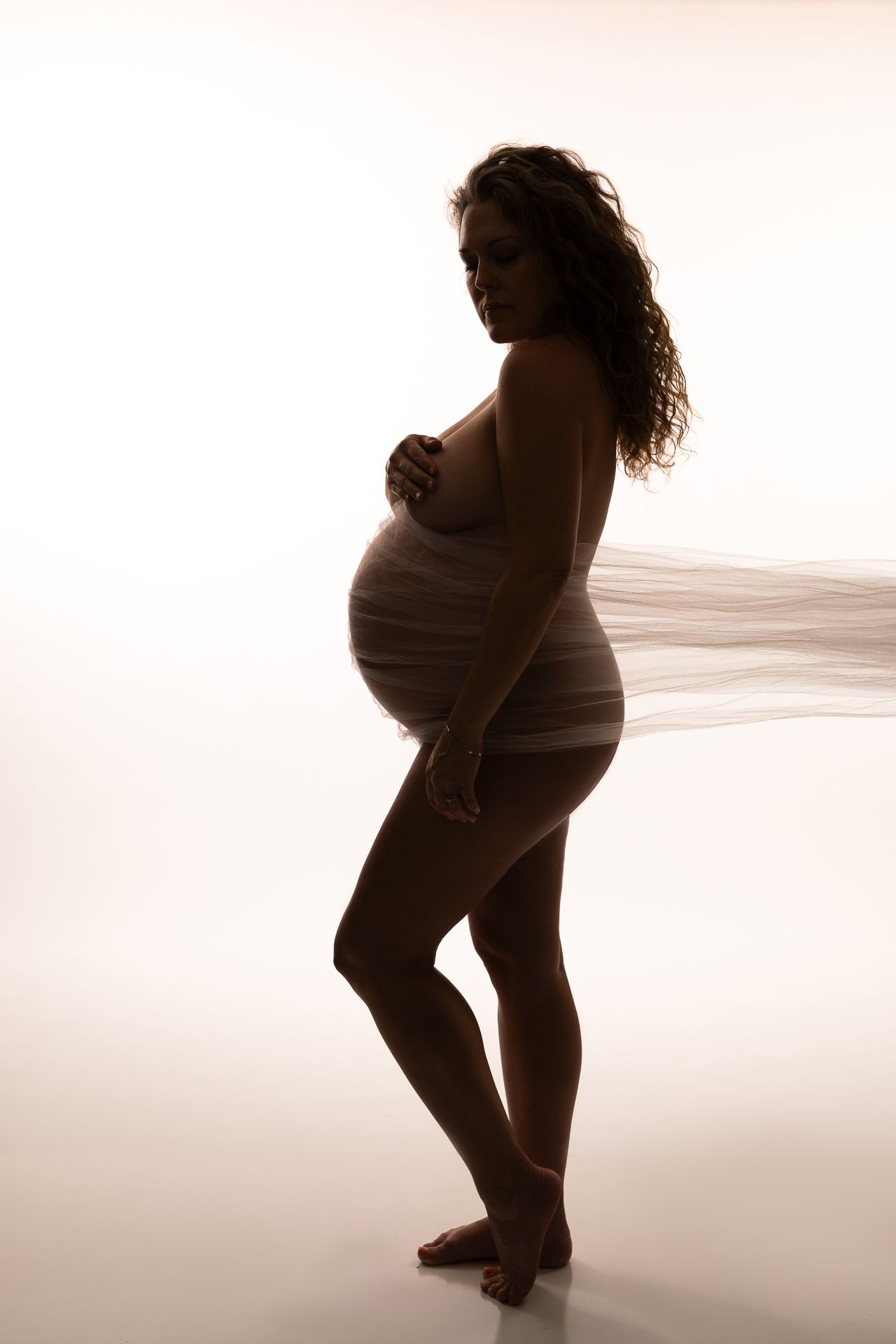 A silhouetted maternity photo series showing a pregnant woman's figure in flowing fabric against a light background in the Bonsall Studio ne