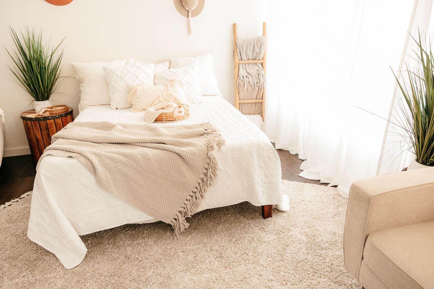 Minimalist boho bedroom with cream bedding, tassel throw, sheer curtains, and potted green plants. in the Bonsall Studio near Fallbrook, Vis