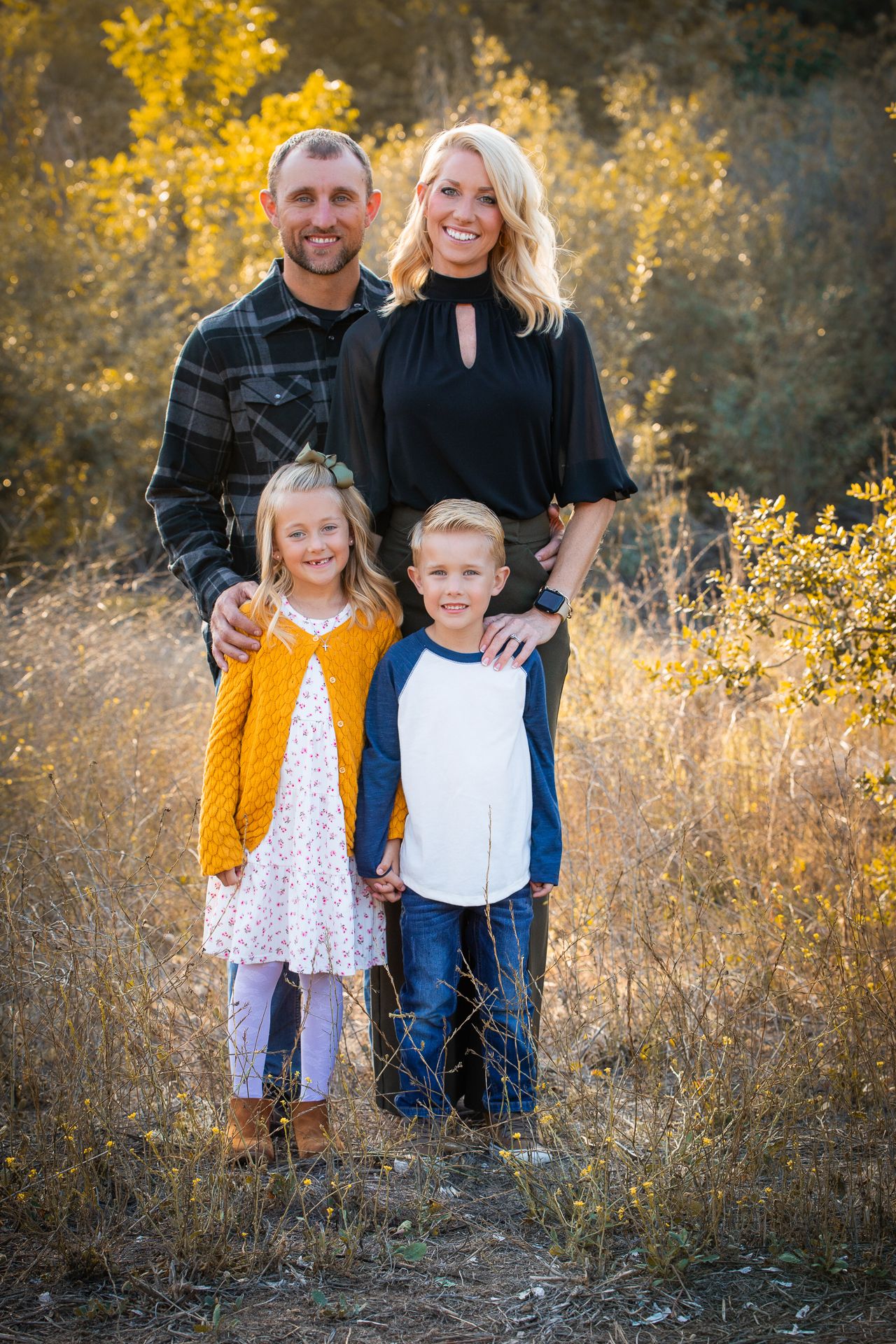 Family of four posing in golden autumn field, parents with two young children at sunset in Bonsall, near Fallbrook, & Temecula