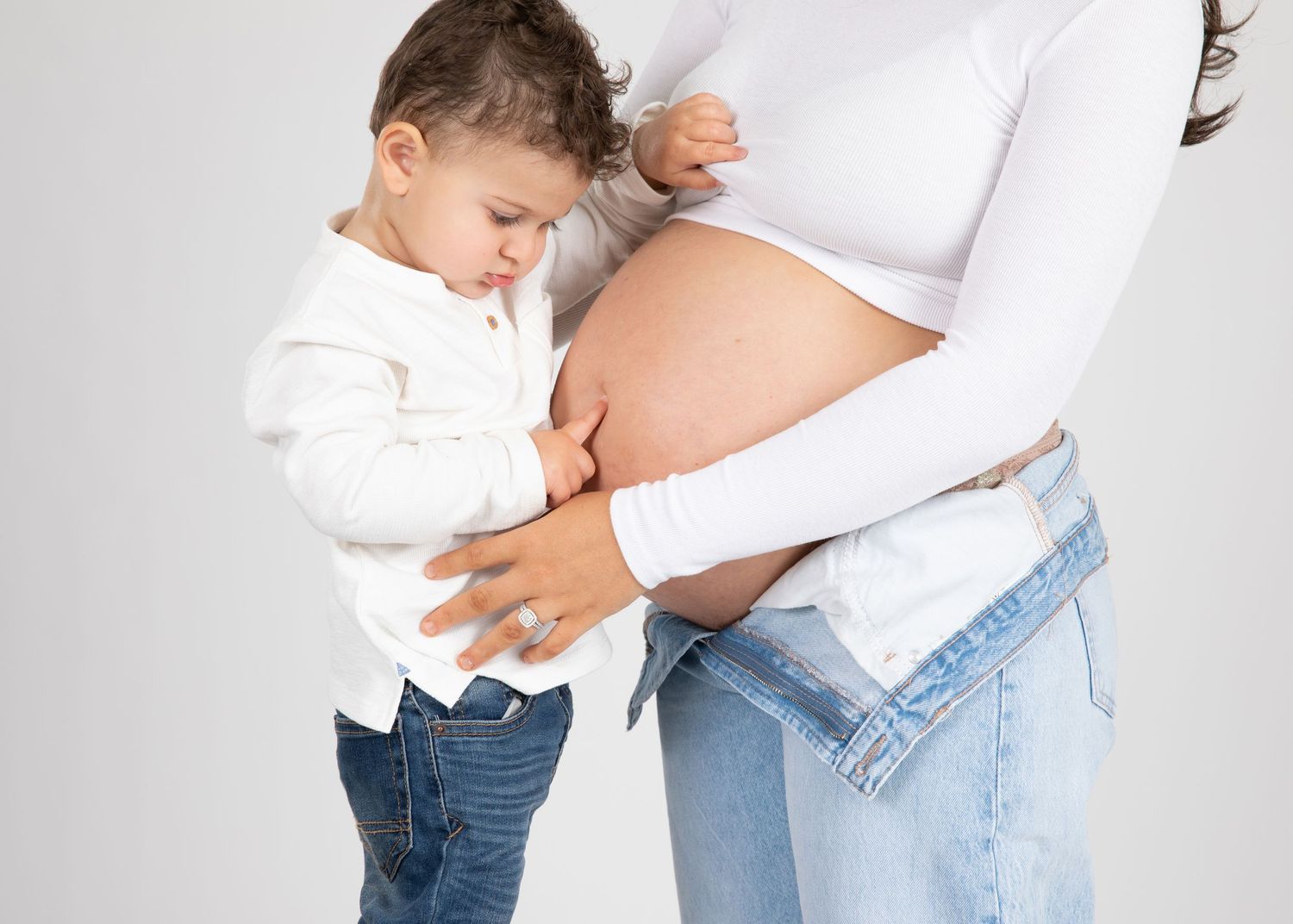 Toddler in white jacket hugging pregnant mothers bare belly bump in Bonsall, near Fallbrook, & Temecula