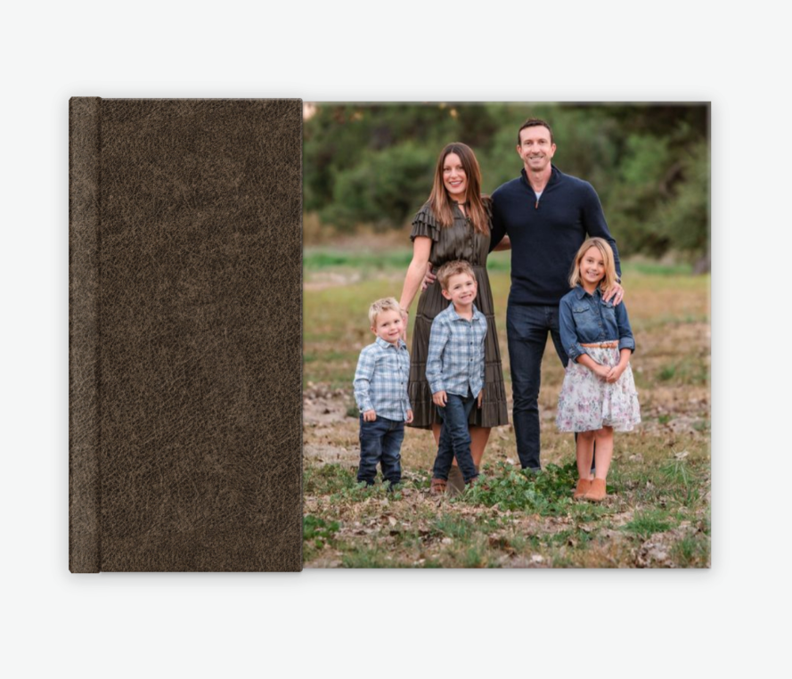 Dark linen landscape photo album with a family portrait cover featuring parents and three young children outdoors.