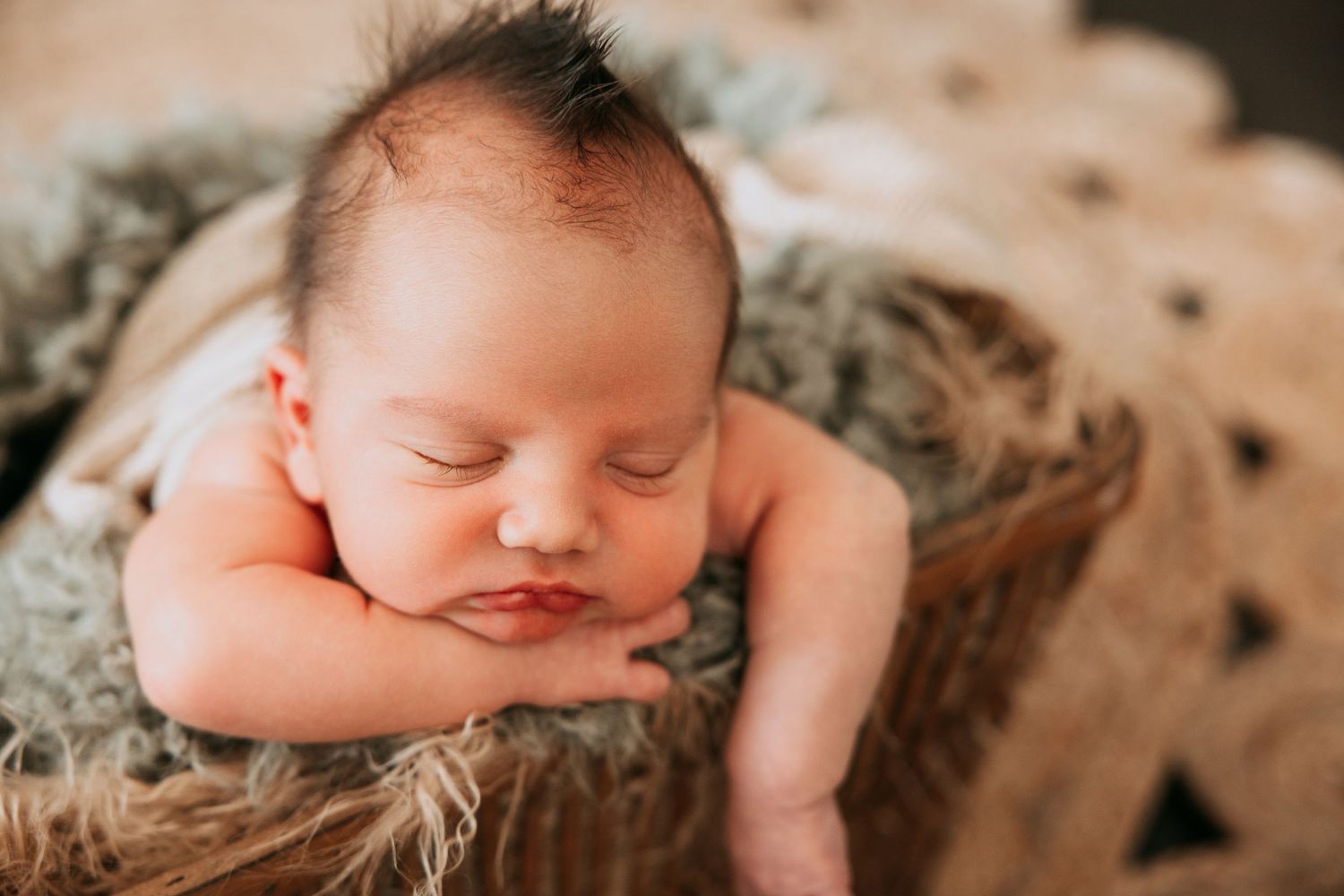 Sleeping newborn baby posed in rustic basket with soft fur during professional newborn photography session.