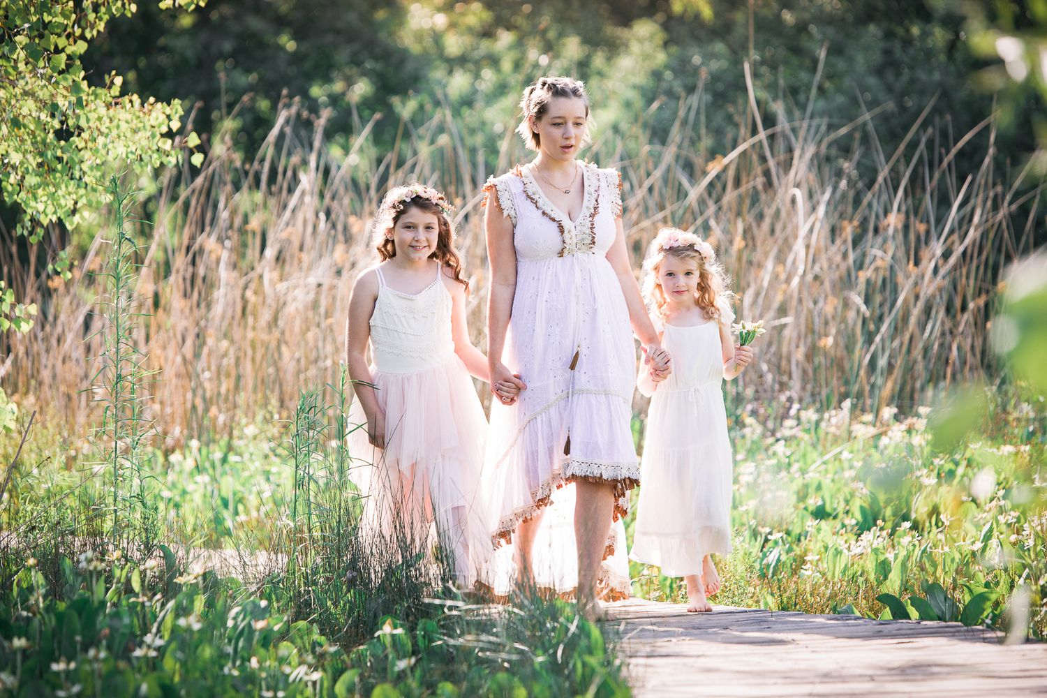 Woman in white dress walks with two young girls in pink dresses on a sunny garden path.  In Bonsall, near Oceanside