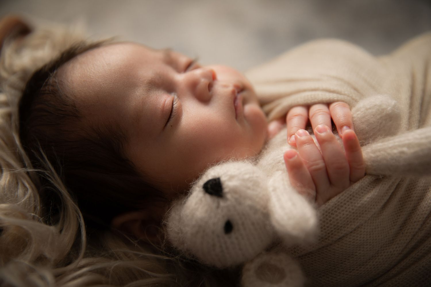 Sleeping newborn baby smiling while holding a small white teddy bear.