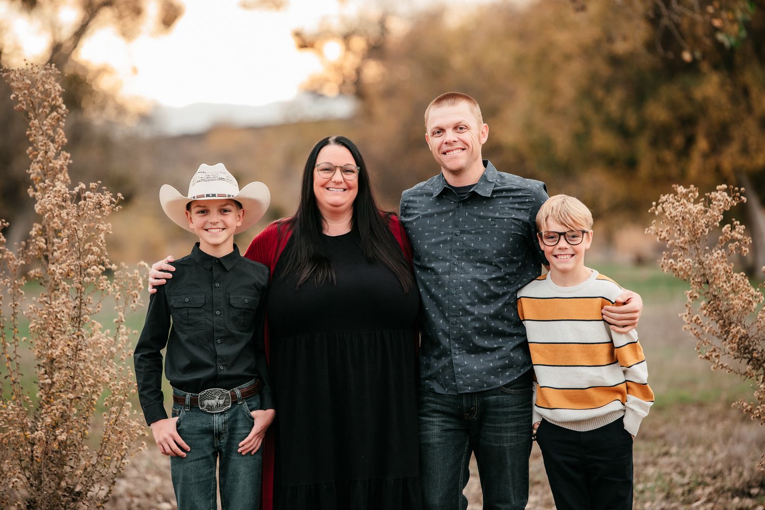 Family of four smiling on autumn path, boys in western and striped shirts with parents.