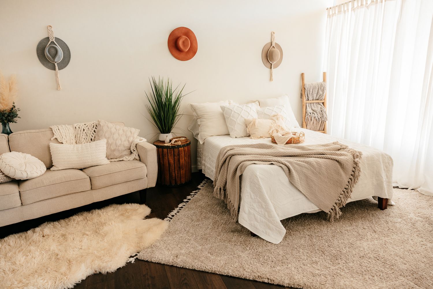 Cozy boho bedroom with neutral bedding, fluffy rug, decorative hats on wall, and a beige sofa. in the Bonsall Studio near Fallbrook, Vista,