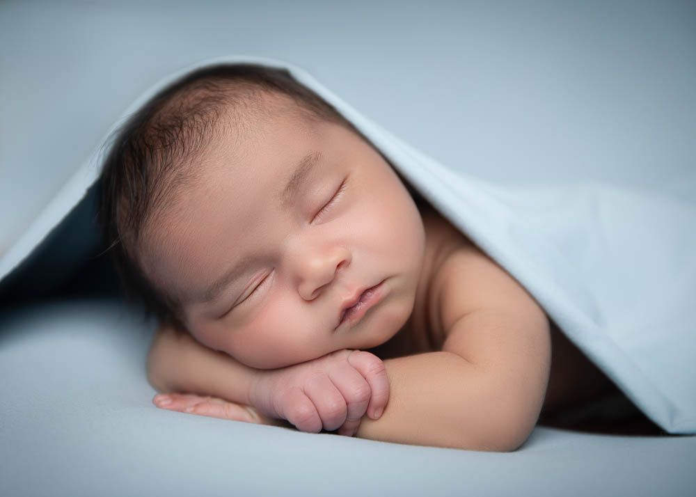 Peaceful newborn baby sleeping under a soft blue blanket in a serene studio portrait in the Bonsall Studio near Fallbrook, Vista, Oceanside