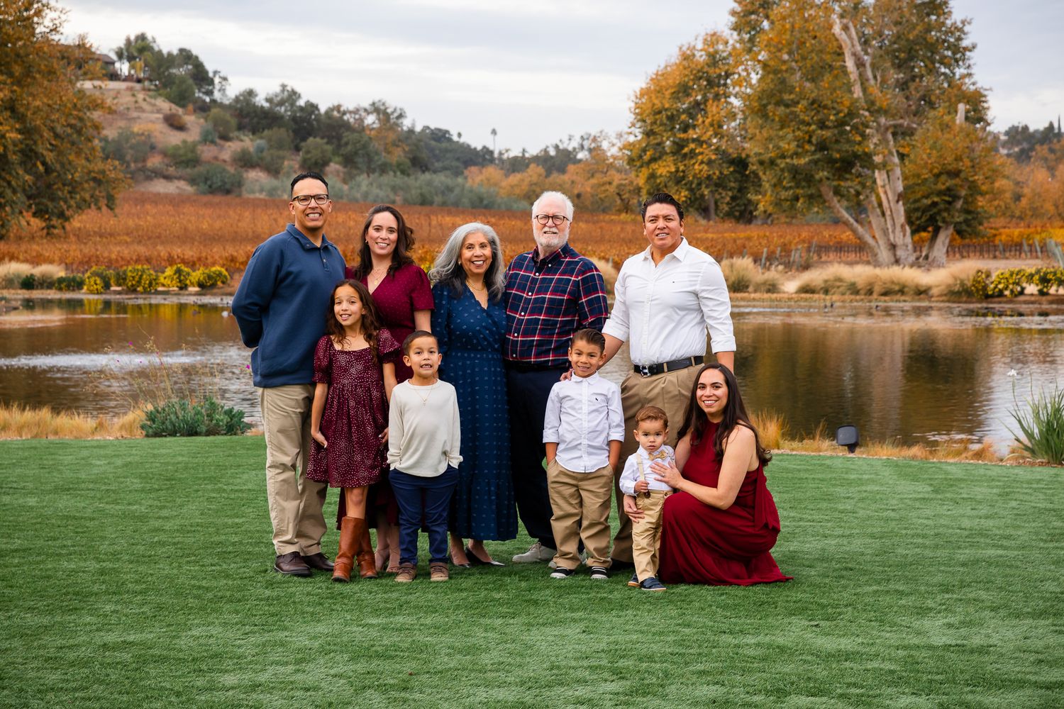 Extended family of nine posing by a pond with fall foliage at Monserate Winery in Fallbrook, CA