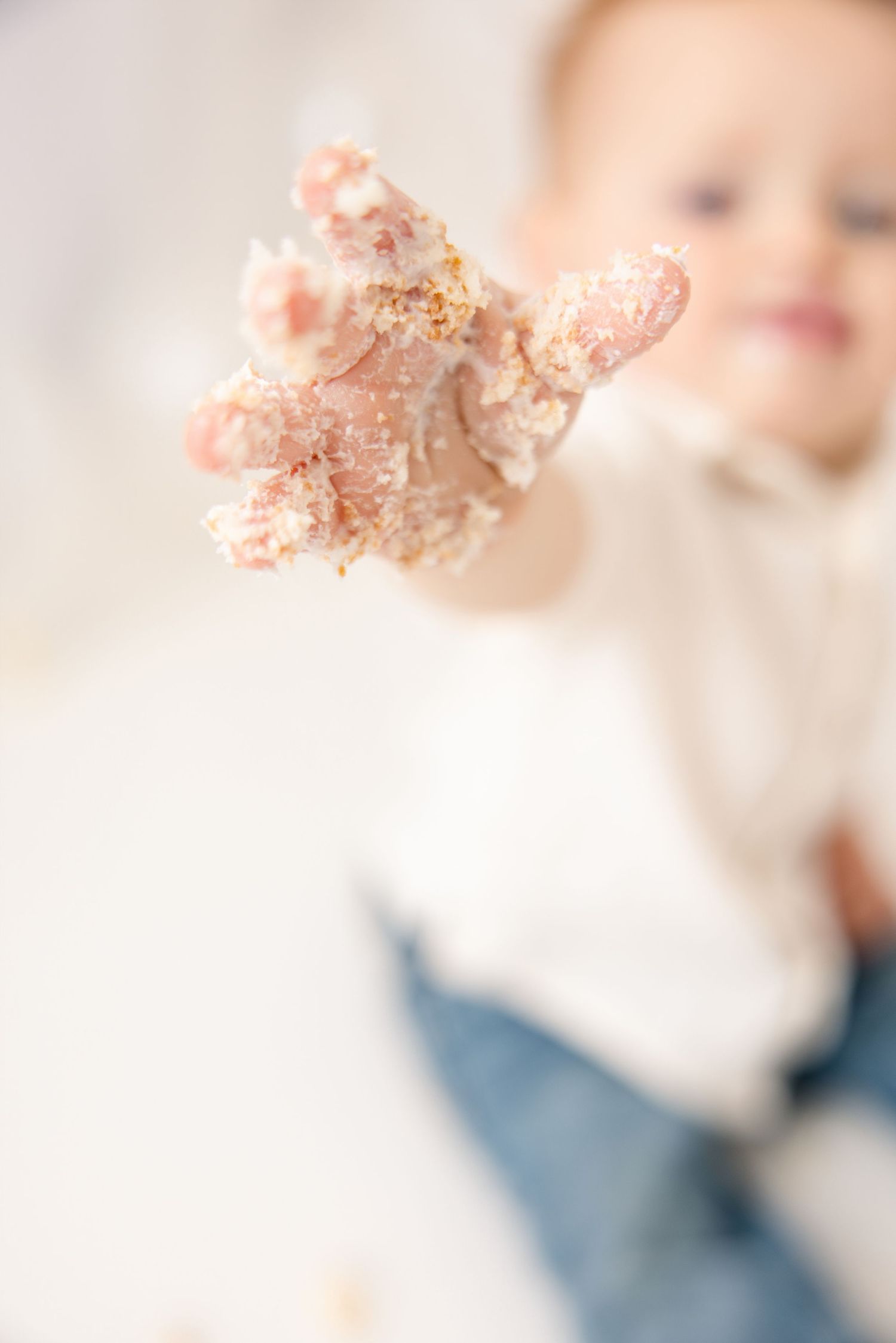 Baby reaching out a frosting-covered hand during a first birthday cake smash photo session.