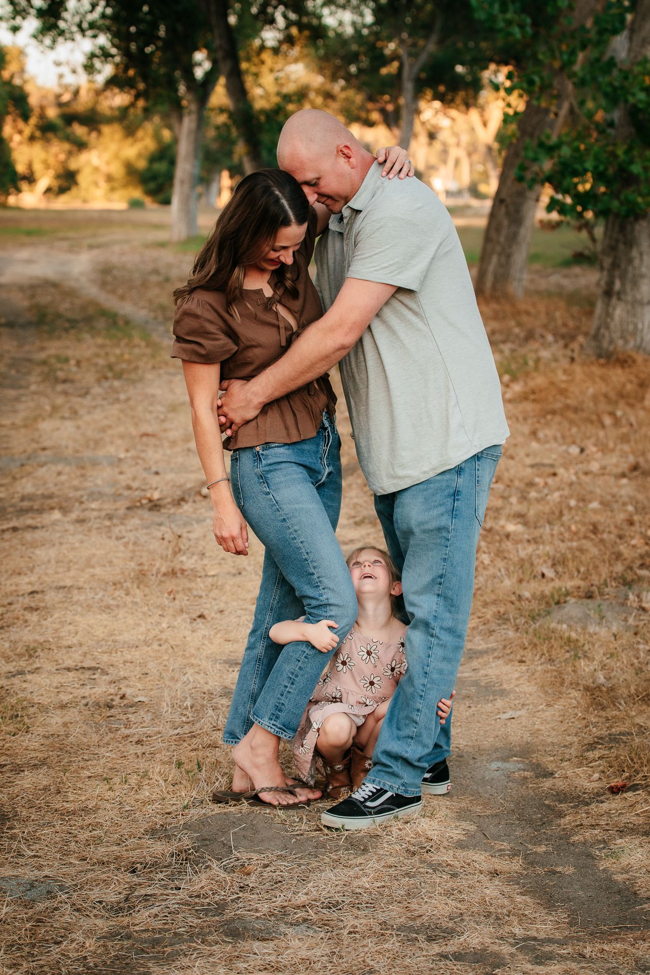 Couple embracing while toddler peeks between their legs at the Bonsall Preserve.