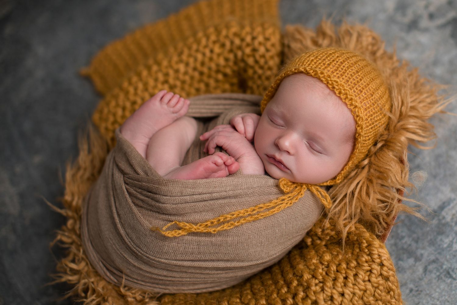 Sleeping newborn baby wrapped in tan cloth with mustard knit bonnet and blanket.