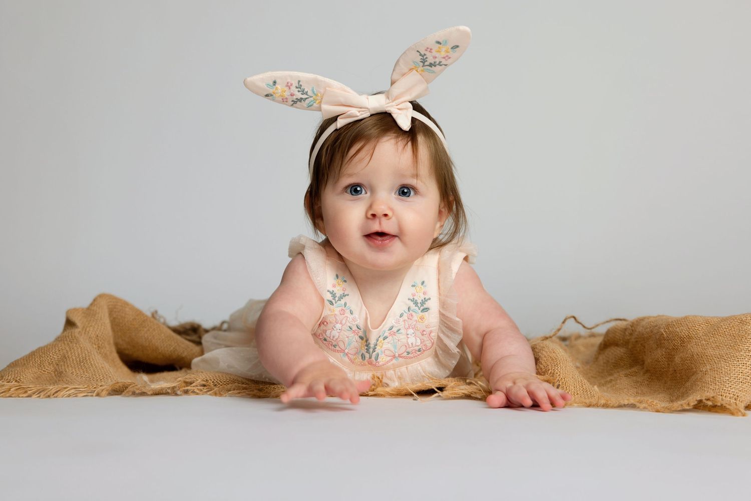 Sweet baby girl wearing bunny ear headband lying on burlap blanket in an Easter-themed photo session. Fallbrook Newborn Photographer