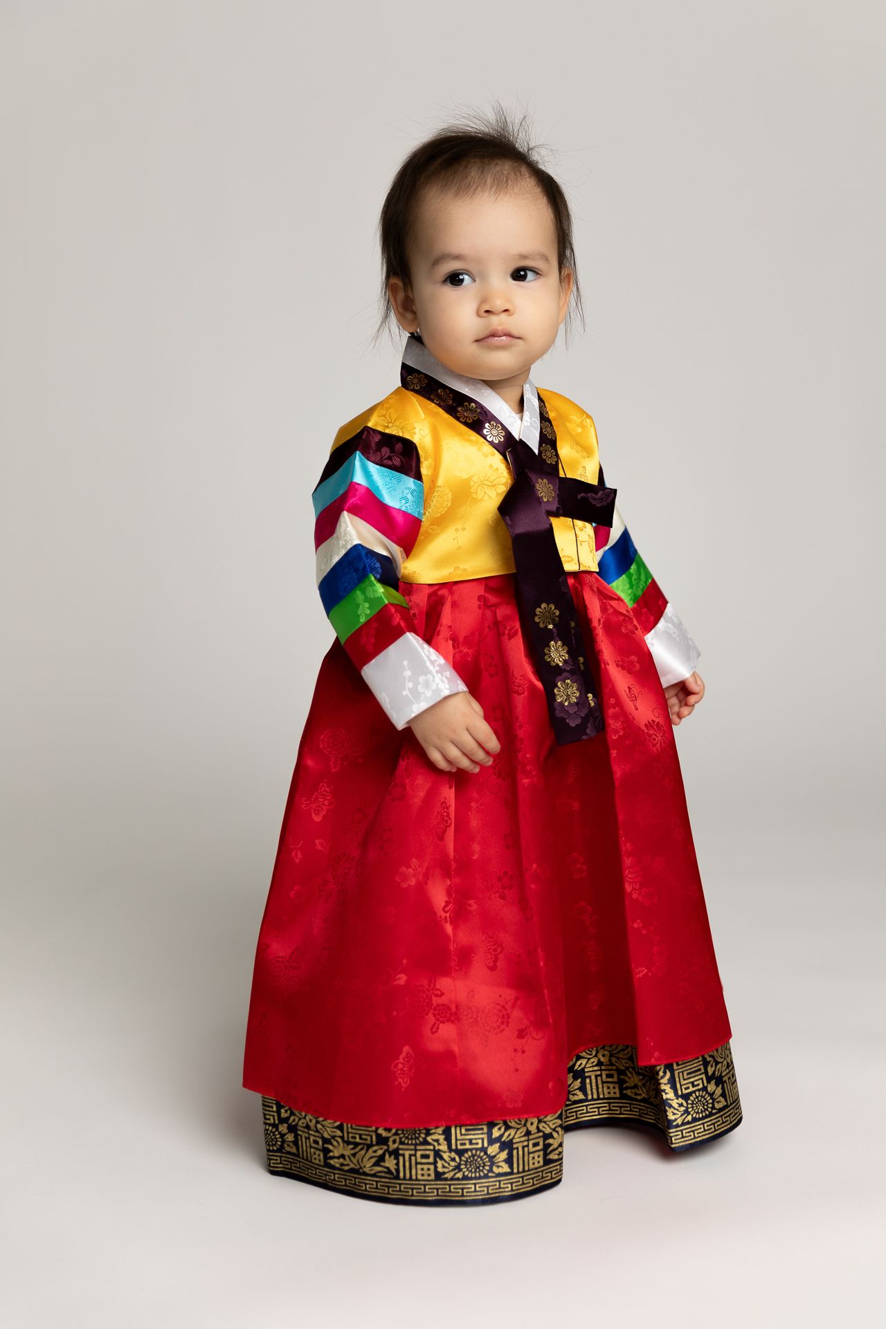 Baby in colorful traditional Korean hanbok standing in studio.