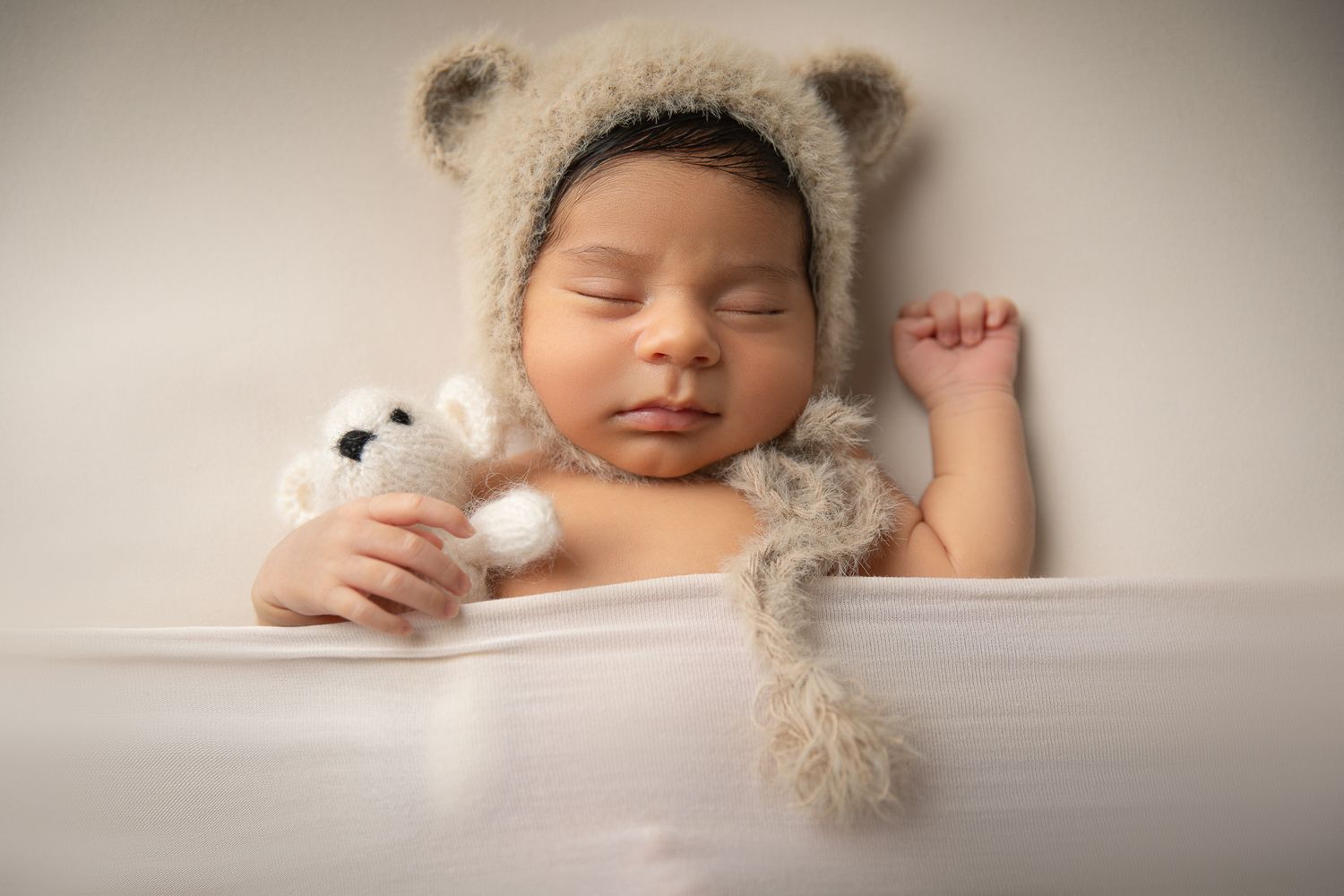 Sleeping newborn baby wearing a knit bear ear bonnet cuddles a tiny teddy bear toy. vista newborn photographer