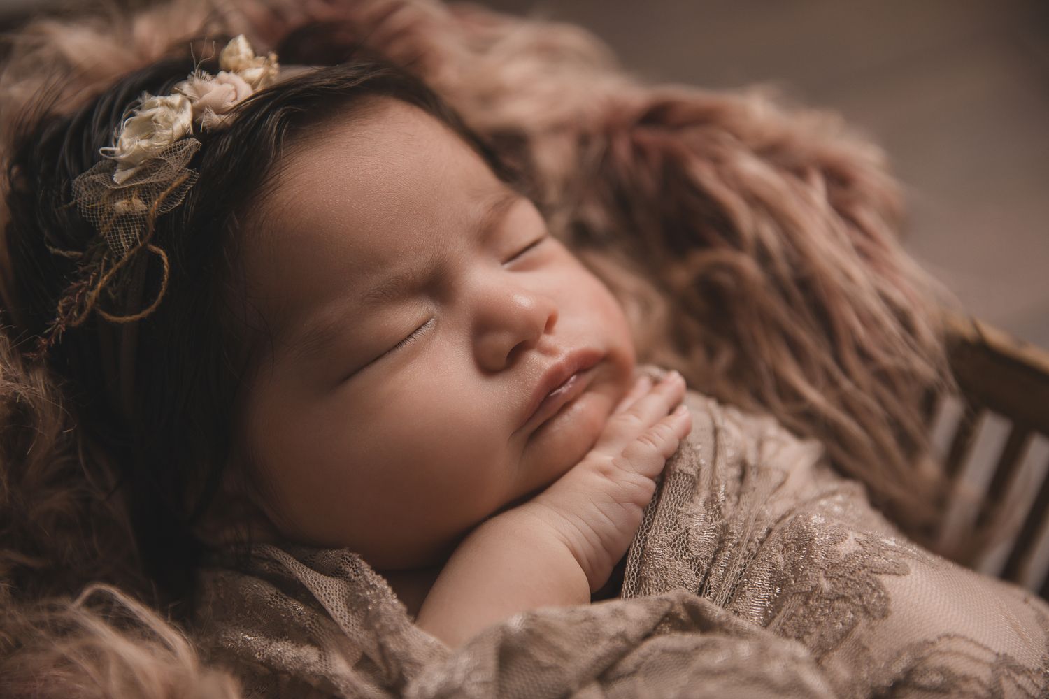 Close-up of a peacefully sleeping newborn baby with dark hair wearing a floral headband in warm tones. vista newborn photographer