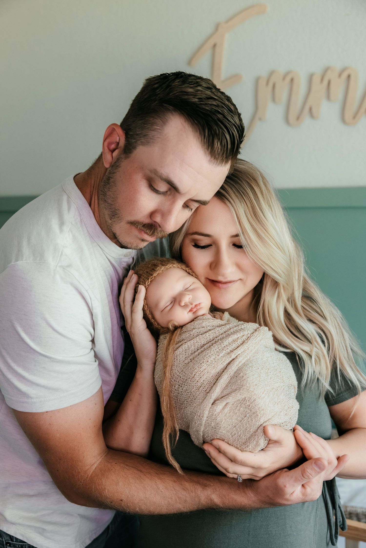 A couple tenderly holds their swaddled newborn baby, eyes closed, sharing a peaceful family moment in a nursery.